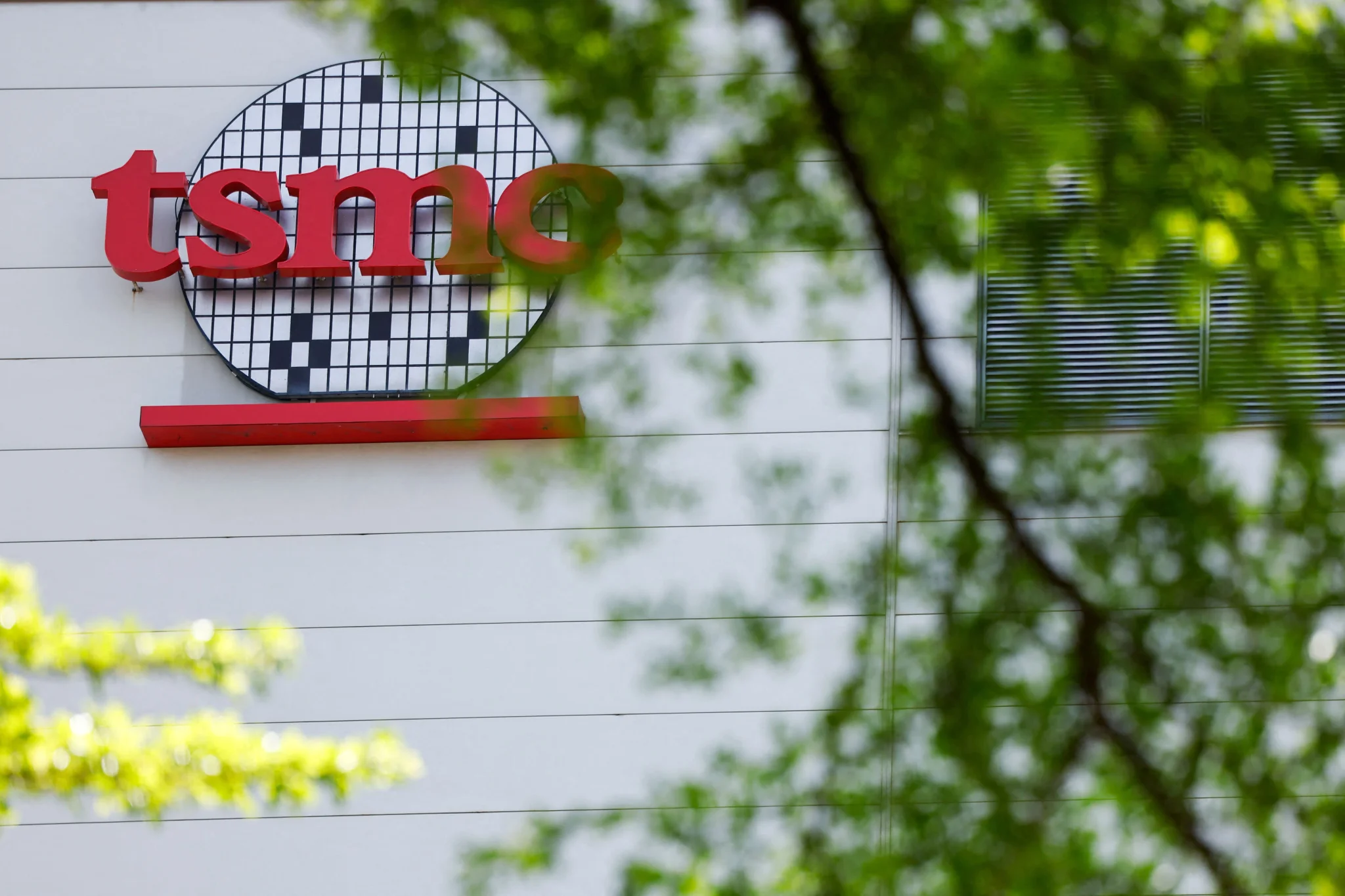 شعار شركة TSMC يظهر بوضوح على واجهة المبنى، محاطاً بأوراق الشجر، مما يعكس دورها المحوري في صناعة الرقائق والتكنولوجيا في آسيا.