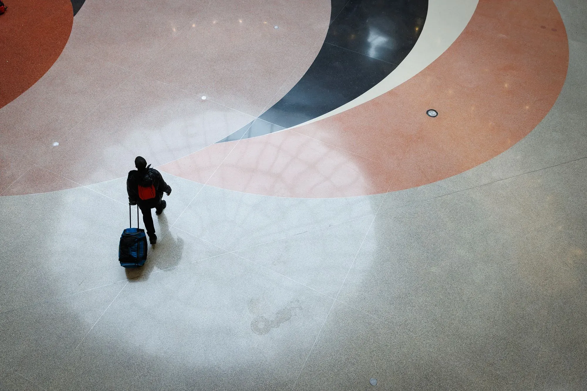 شخص يحمل حقيبة سفر ويتجه نحو منطقة دائرية ملونة في مطار، مما يعكس تجربة الانتقال والتخطيط للتقاعد في الخارج.