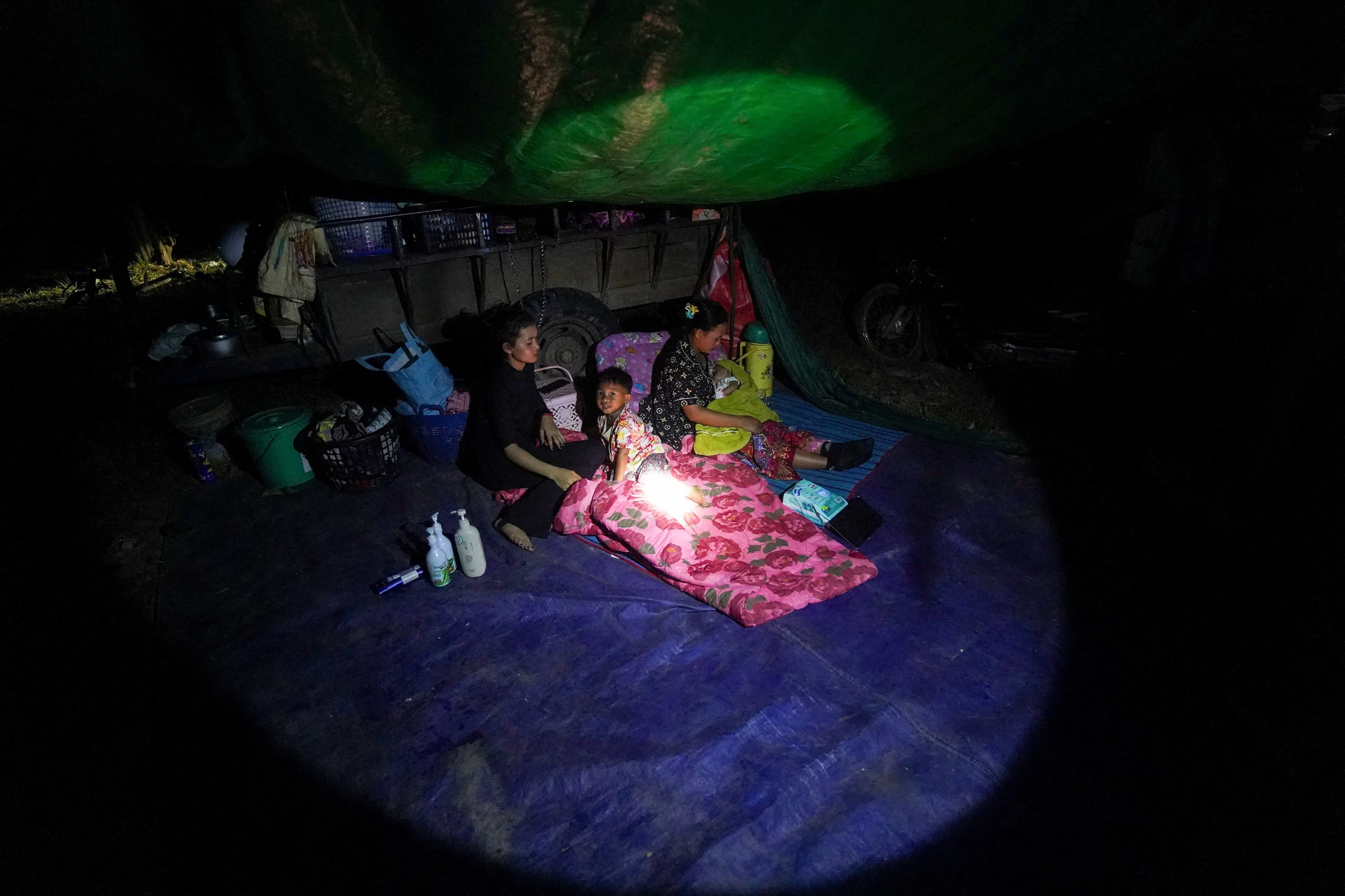 عائلة تتجمع تحت غطاء في الظلام، حيث تضيء مصباح يدوي وجه طفل صغير، مما يعكس تأثير النزاع المسلح على المدنيين.