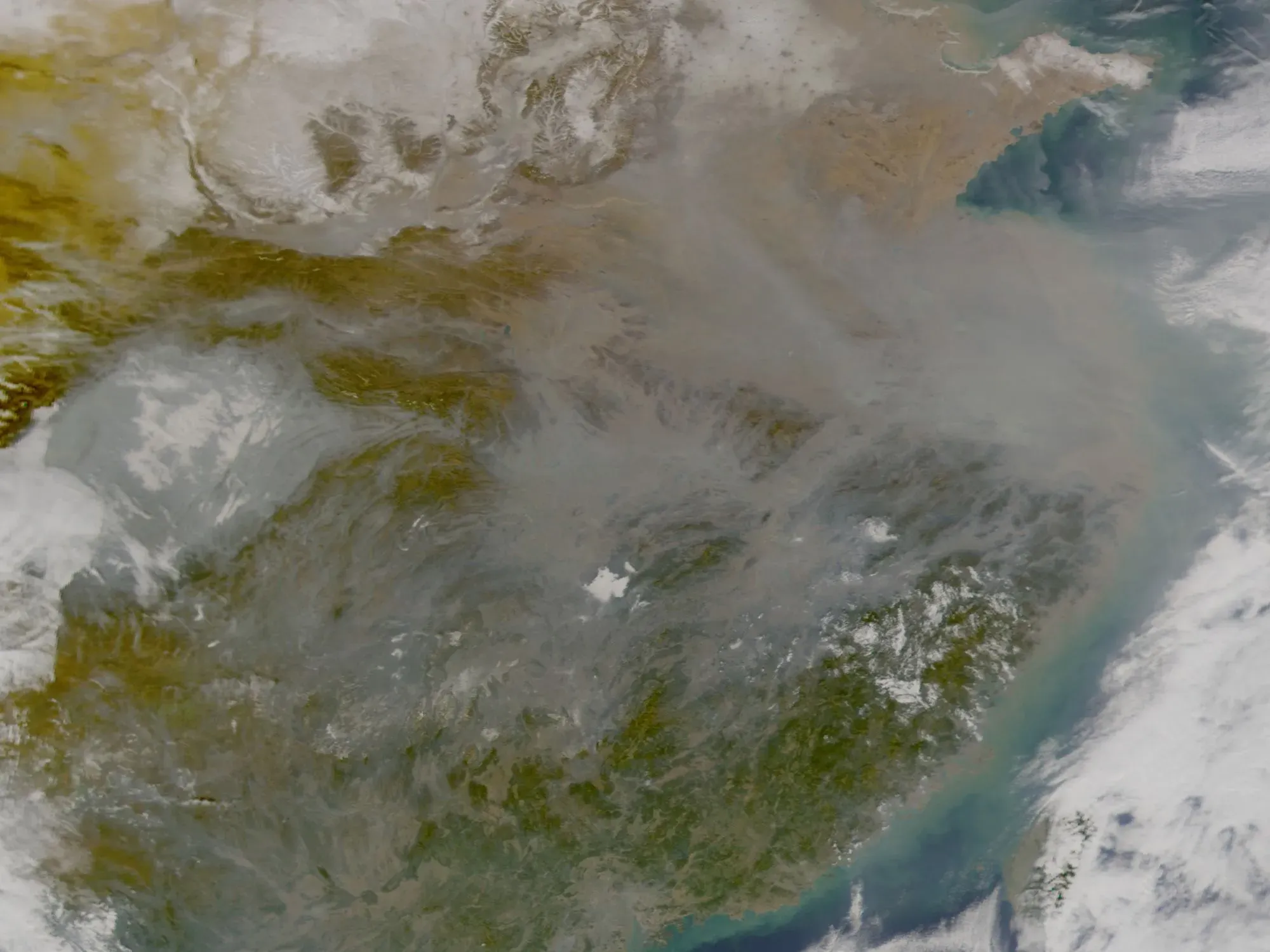 صورة فضائية تُظهر تلوث الهواء فوق منطقة جبلية، مع غيوم وطبقات من الضباب، مما يعكس تأثير مركبات الكربون الكلورية فلورية على المناخ.