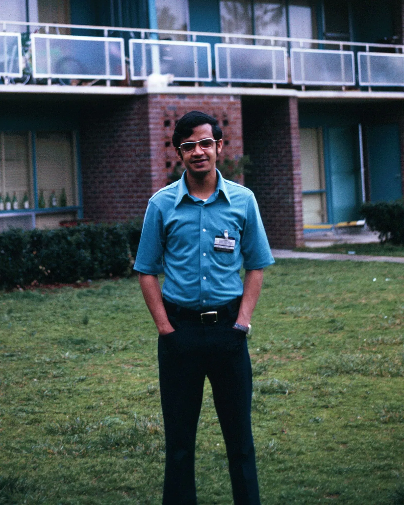 شاب يرتدي قميصًا أزرق ويقف في حديقة أمام مبنى سكني، يعكس بداية مسيرته العلمية في مجال علوم المناخ.