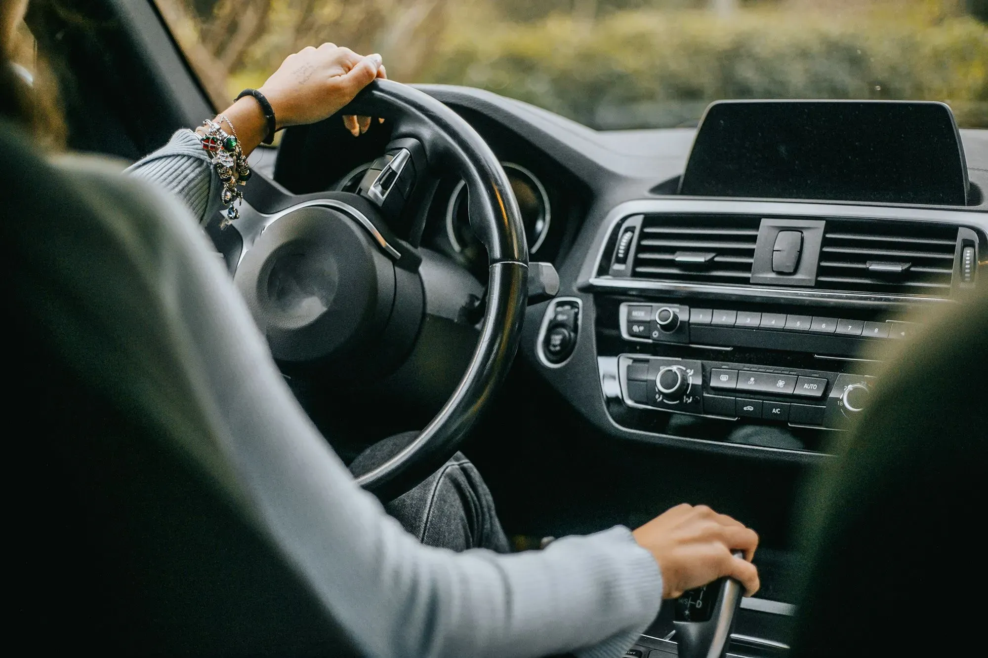 يد تظهر يد سائق يتحكم بعجلة القيادة في سيارة، مع التركيز على لوحة التحكم الداخلية، مما يبرز مصدر التلوث البلاستيكي في الأماكن المغلقة.