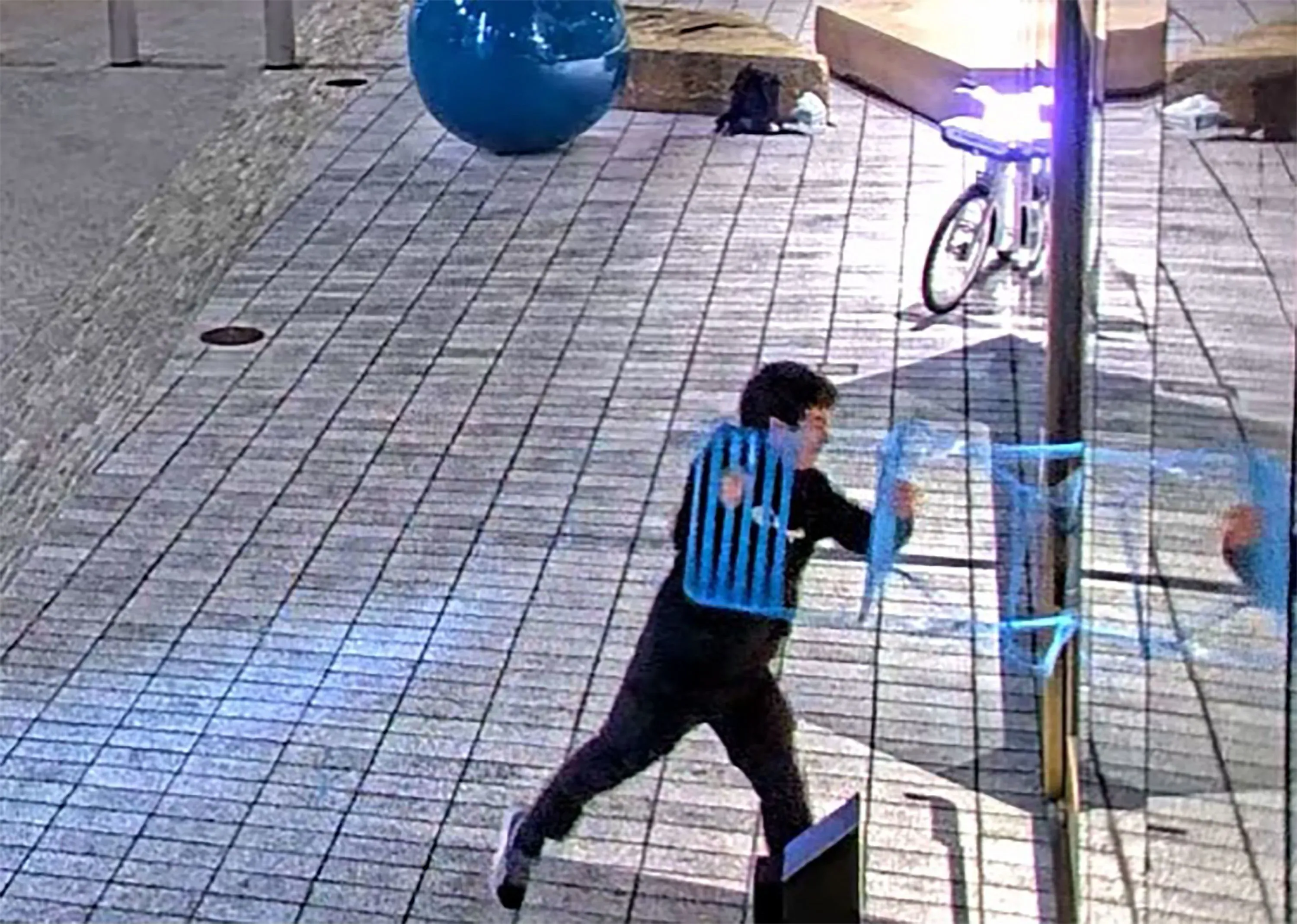 شاب يهاجم بكرسي بلاستيكي عمود إنارة في منطقة عامة، مع وجود دراجة خلفه، في سياق تصاعد التوترات حول الذكاء الاصطناعي.