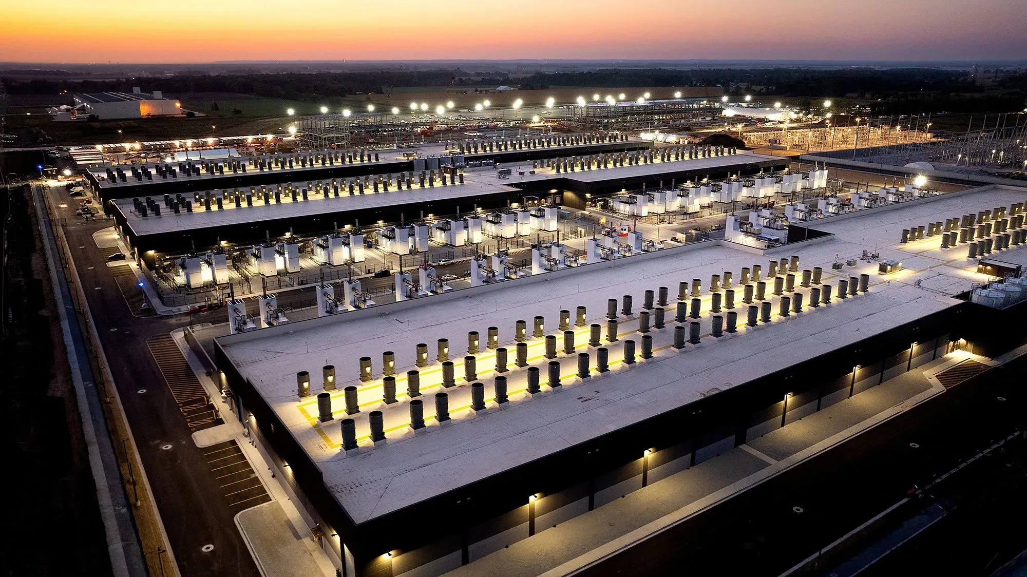 مركز بيانات ضخم مزود بأجهزة متطورة، يضيء ليلاً، يمثل استثمار التكنولوجيا في البنية التحتية للذكاء الاصطناعي.