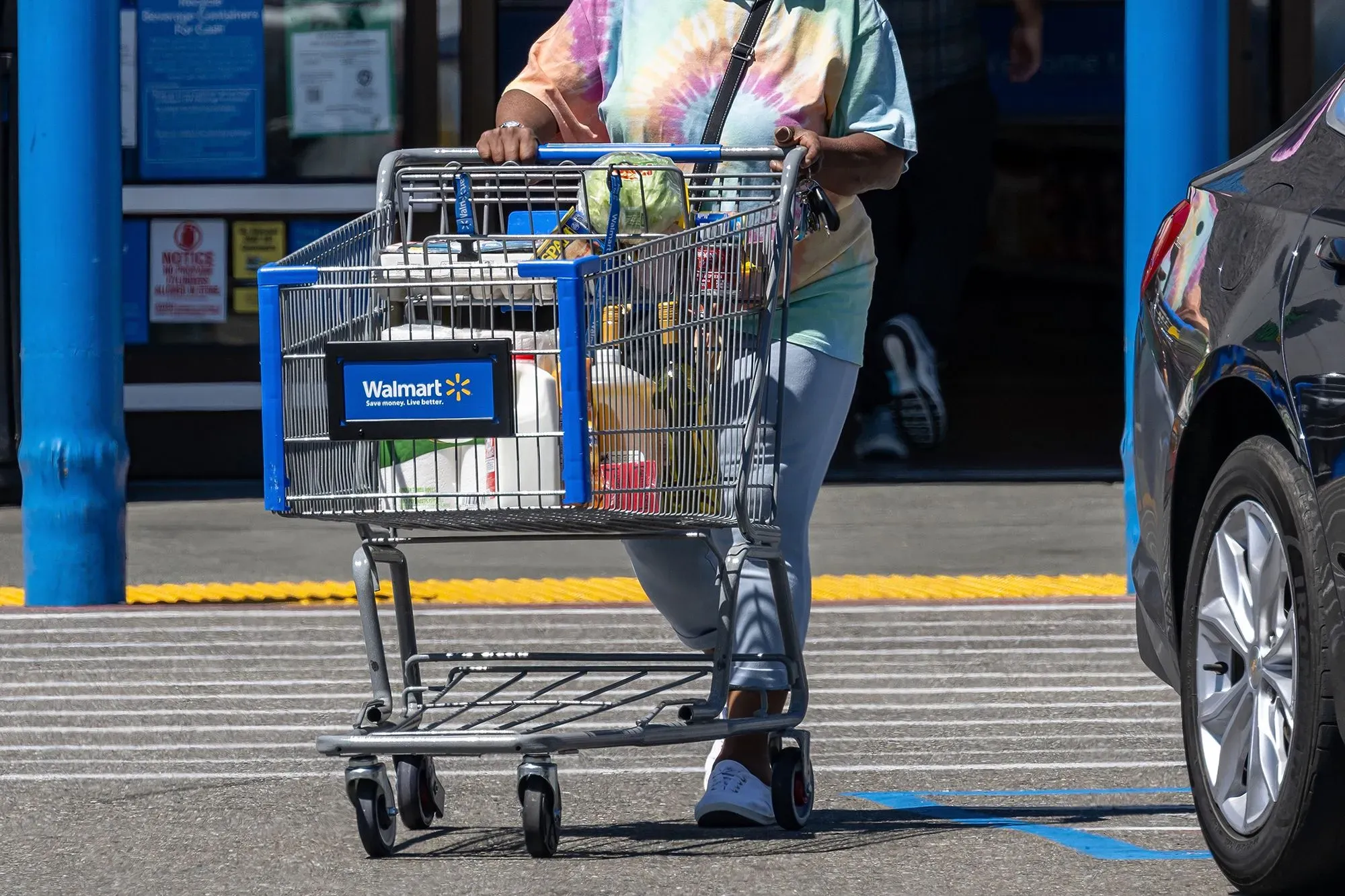 امرأة تحمل عربة تسوق خارج متجر وول مارت، تعكس زيادة الإقبال على التسوق بسبب البحث عن القيمة والصفقات.