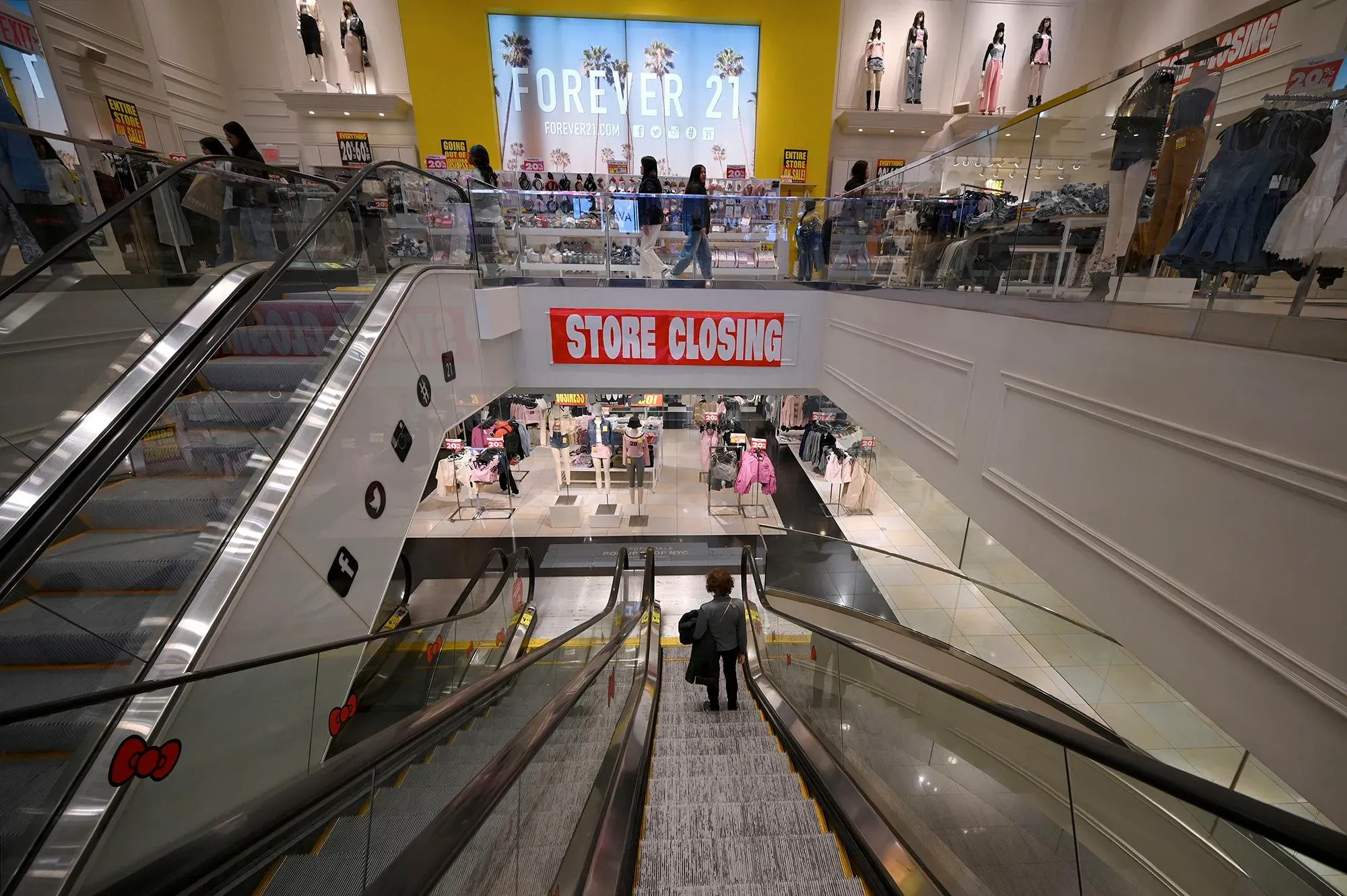 متجر Forever 21 مغلق، مع لافتة "إغلاق المتجر" واضحة، بينما ينزل المتسوقون على السلم الكهربائي. تشير الصورة إلى تراجع العلامة التجارية في عام 2025.