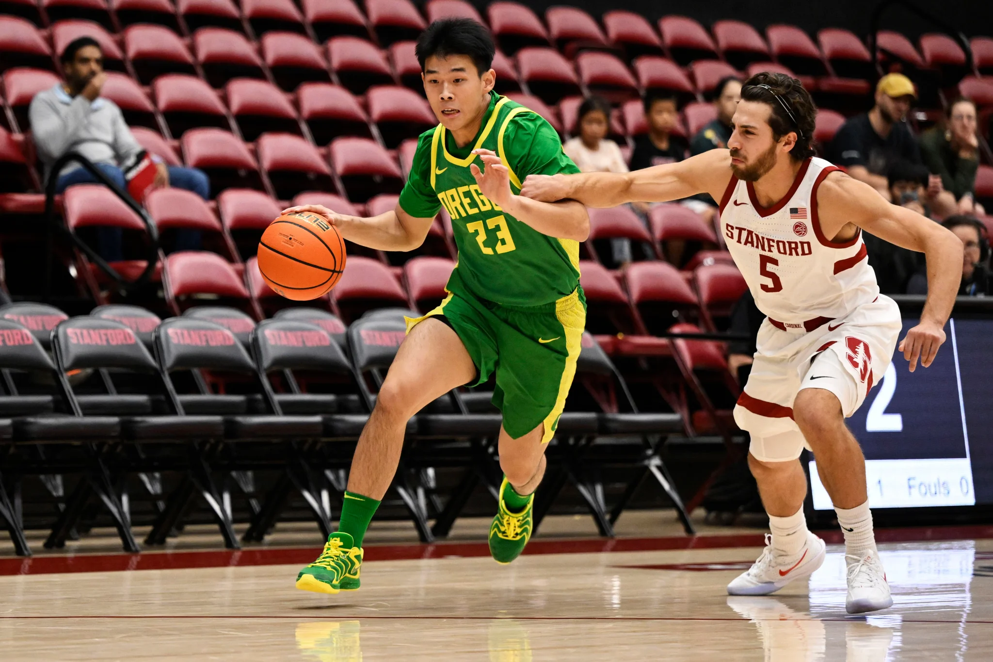 لاعب كرة سلة صيني يرتدي زي أوريغون يراوغ لاعب ستانفورد في مباراة NCAA، يعكس تصاعد حضور اللاعبين الصينيين في الدوري الأمريكي الجامعي.
