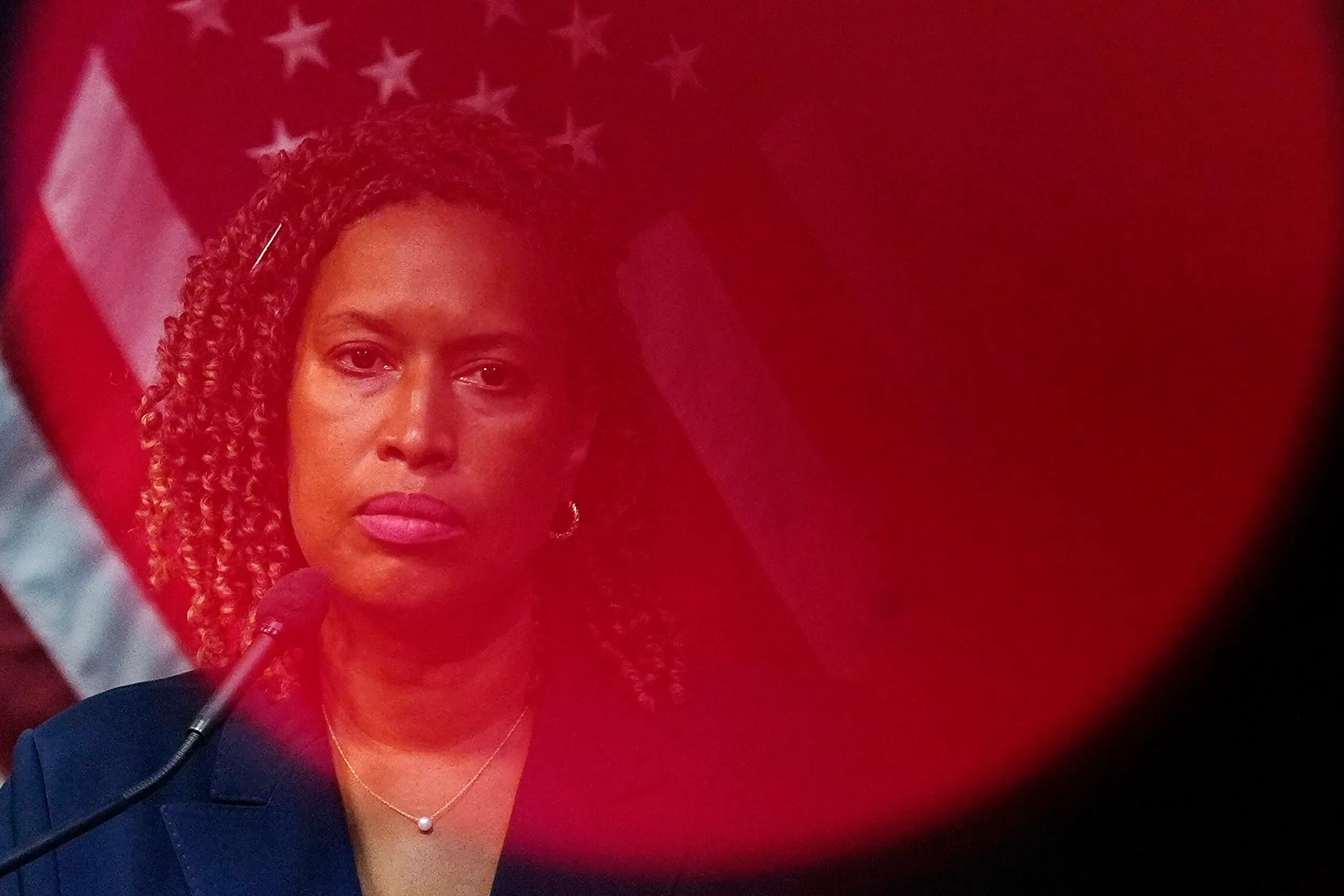 صورة لامرأة ذات شعر مجعد، تبدو جادة، تتحدث من خلف ميكروفون، مع العلم الأمريكي خلفها. تعكس الصورة أجواء سياسية مشحونة.
