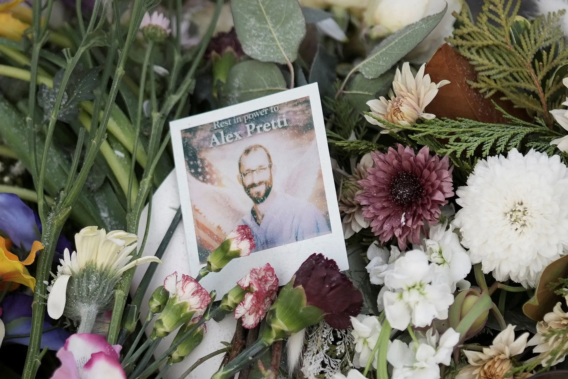 باقة من الزهور مع صورة تذكارية لأليكس بريتي، تعبير عن الحزن والاحترام بعد وفاته، وسط أجواء من التأمل والمواساة.