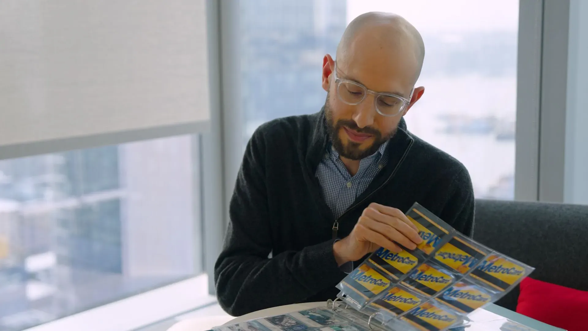 شخص يجلس على أريكة، يتصفح ألبومًا يحتوي على بطاقات مترو نيويورك، مستعرضًا تصميماتها المتنوعة.