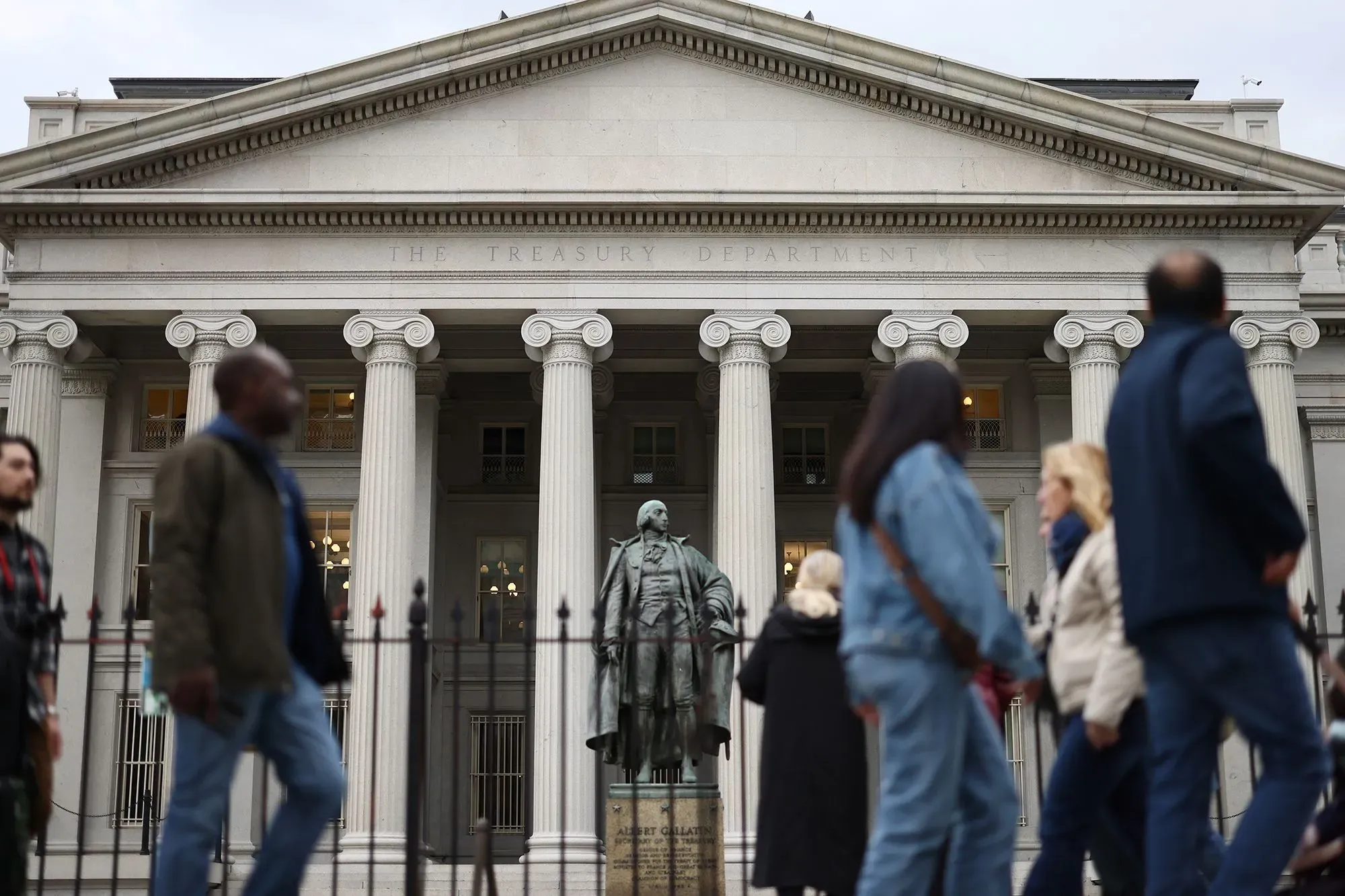 واجهة وزارة الخزانة الأمريكية مع تمثال لألكسندر هاملتون، ومارة يتجولون في المنطقة، مما يعكس النشاط الاقتصادي.