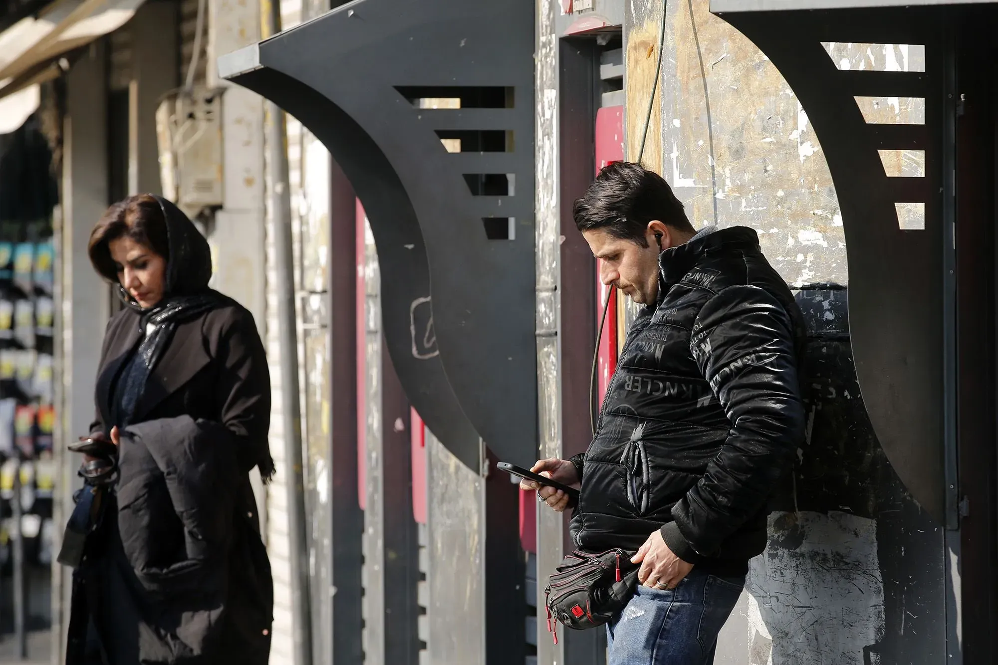 امرأة ورجل يقفان في الشارع، كل منهما يستخدم هاتفه المحمول، مما يعكس تأثير التعتيم الرقمي في إيران.