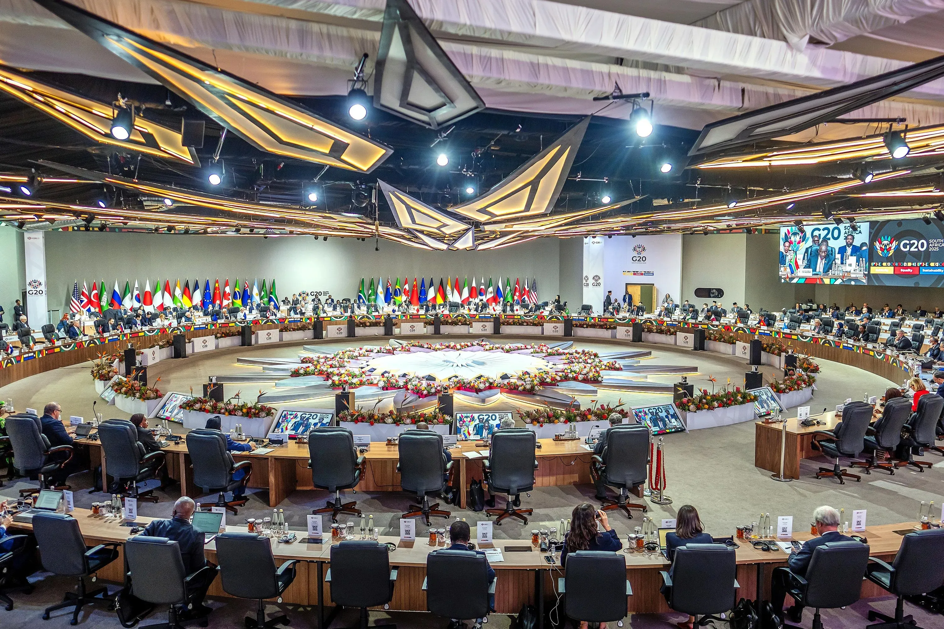 اجتماع قادة مجموعة العشرين في جنوب أفريقيا، حيث يظهر المشاركون في قاعة النقاش وسط أعلام الدول المشاركة وزهور الزينة.