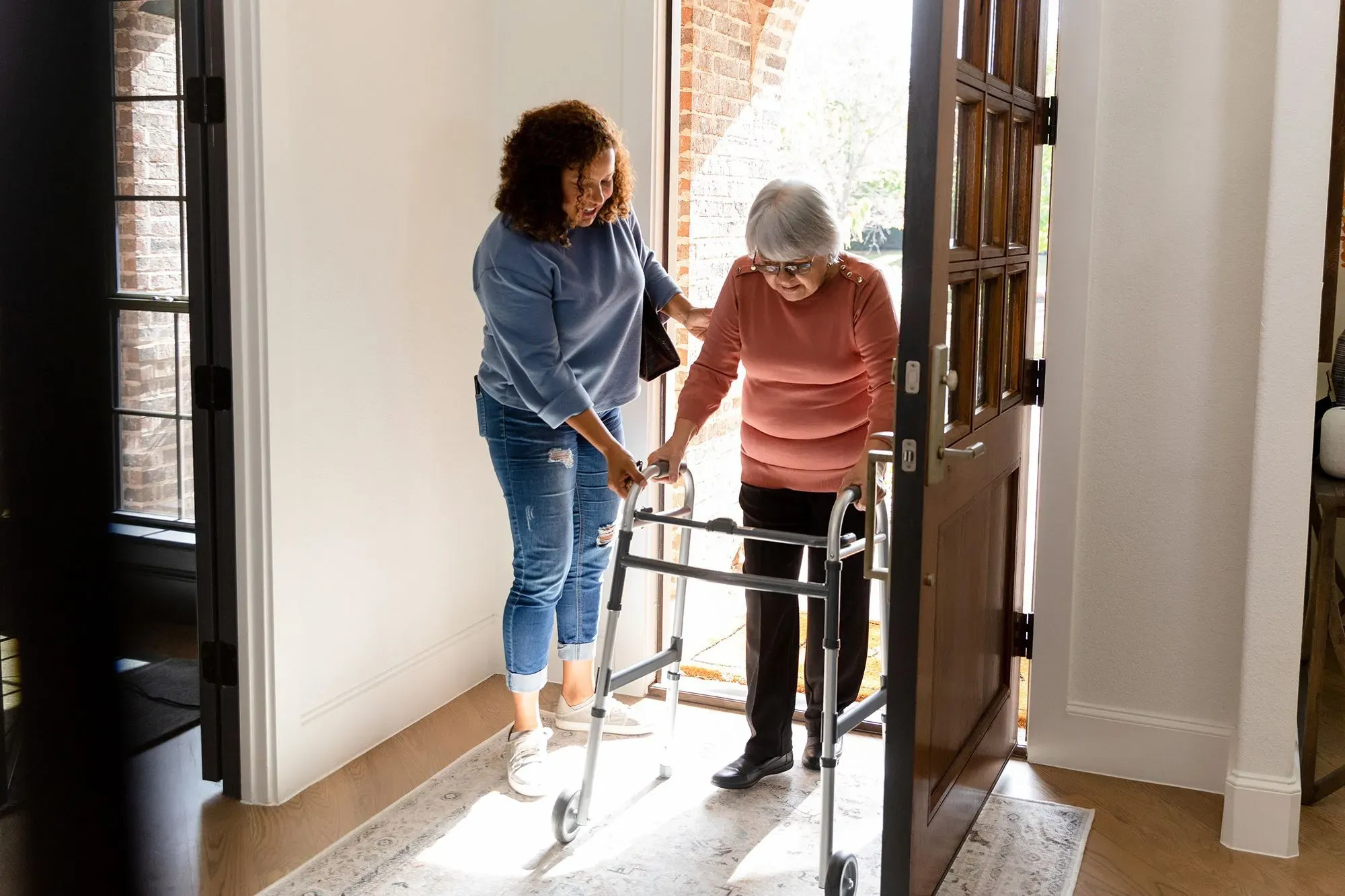 امرأة تساعد مسنّة على استخدام المشاية أثناء الخروج من المنزل، مما يعكس أهمية رعاية كبار السن ودور مقدمي الرعاية.