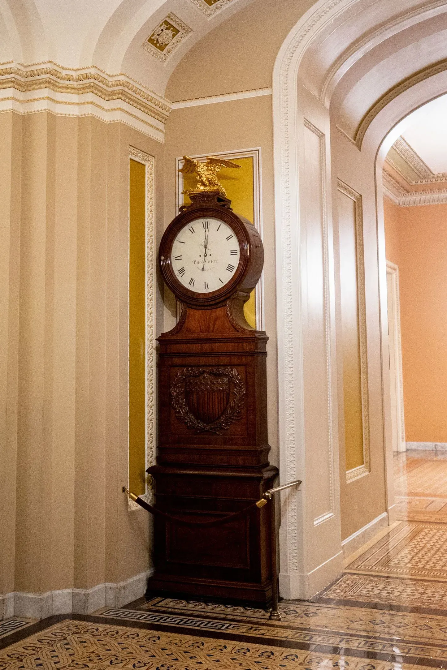 ساعة خشبية تقليدية مزينة بنسر ذهبي، تقع في ممر مبنى حكومي، تعكس تاريخ السياسة الأمريكية وسط تصاعد التوترات بين الحزبين.