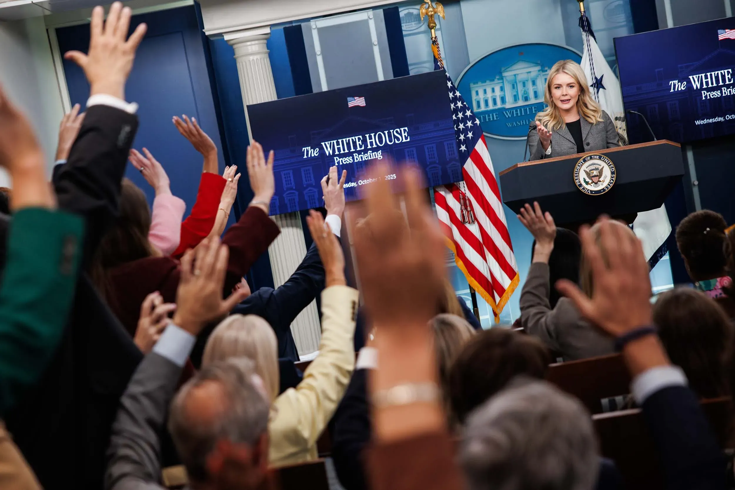 مؤتمر صحفي في البيت الأبيض، حيث ترفع العديد من الأيادي لطرح الأسئلة، بينما تتحدث المتحدثة باسم البيت الأبيض.