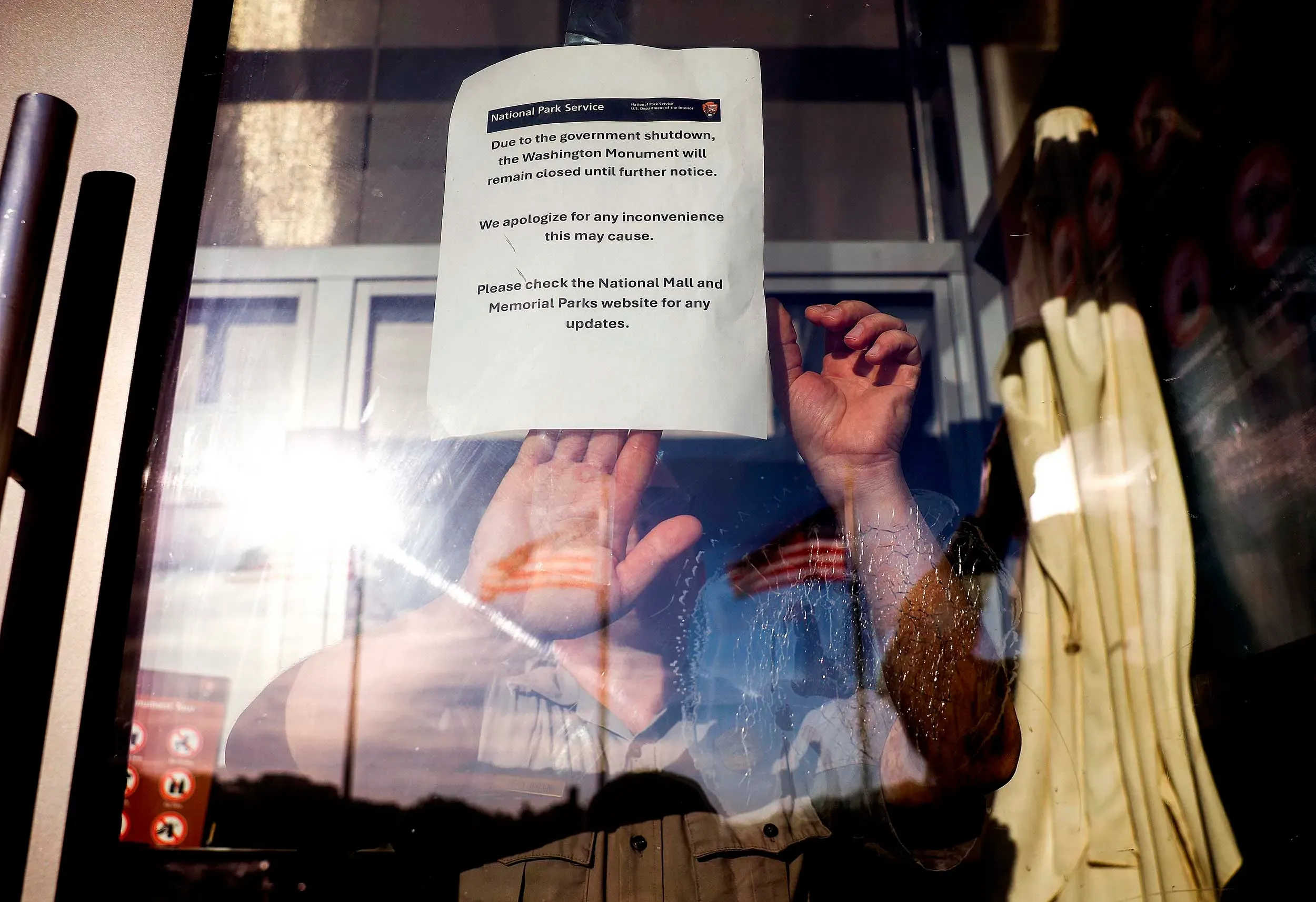 شخص يضع يده على نافذة مغلقة تحمل لافتة تُعلن عن إغلاق نصب واشنطن بسبب الإغلاق الحكومي، مما يعكس تأثير الأزمة السياسية.