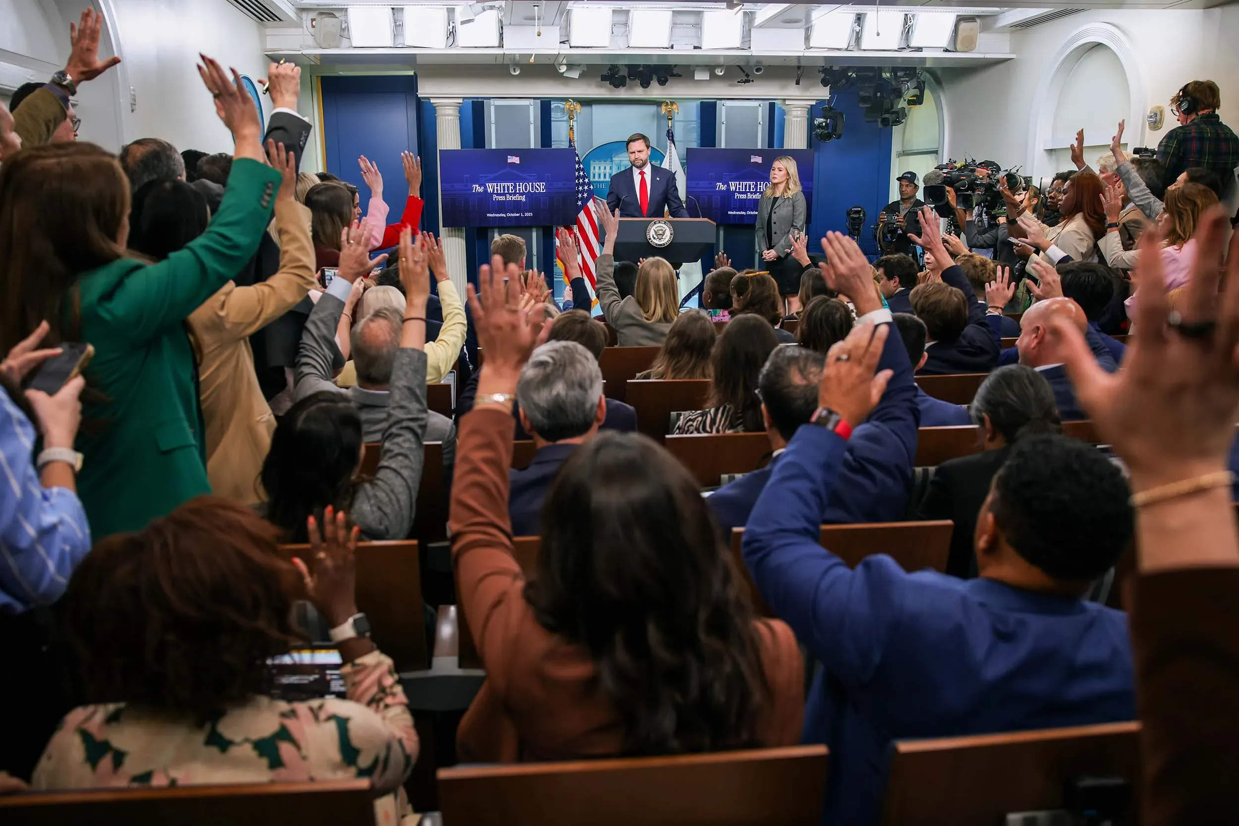 تجمع صحفيون في قاعة المؤتمرات بالبيت الأبيض، يرفعون أيديهم لطرح الأسئلة، وسط أجواء من التوتر السياسي حول الإغلاق الحكومي.