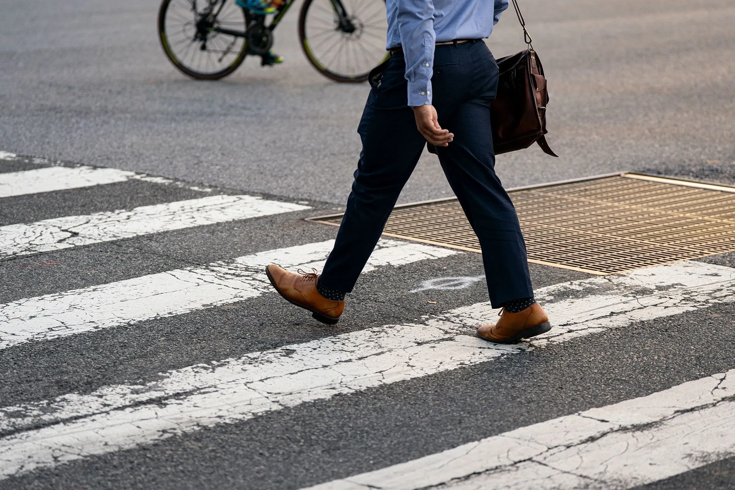 رجل يرتدي بدلة رسمية يسير عبر ممر المشاة في مدينة مزدحمة، بينما يمر دراج خلفه، مما يعكس الحياة اليومية بعد الإغلاق الحكومي.