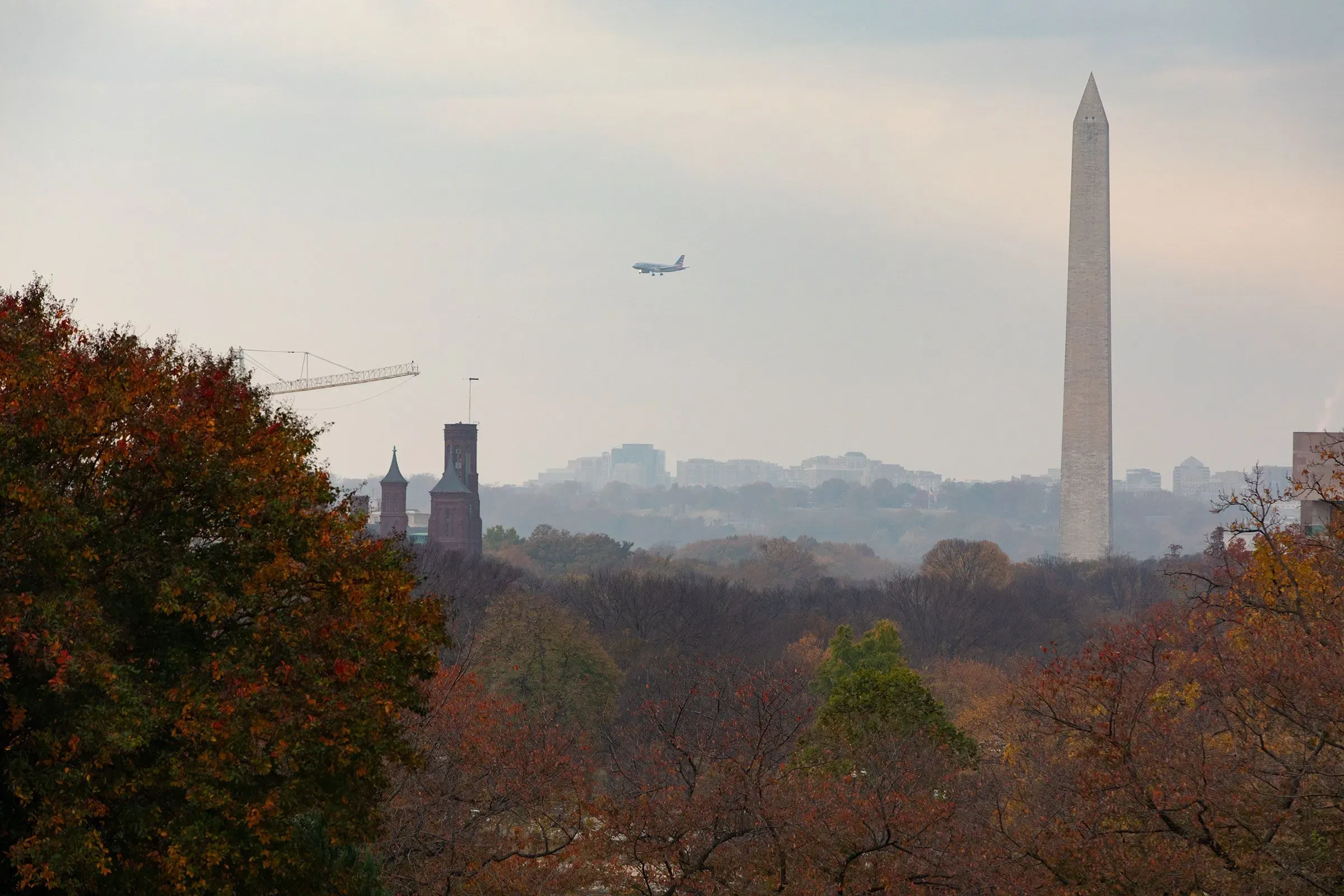 طائرة تحلق فوق معلم واشنطن، بينما تظهر الأشجار الملونة في المقدمة، مما يعكس التأثيرات المستمرة للإغلاق الحكومي.