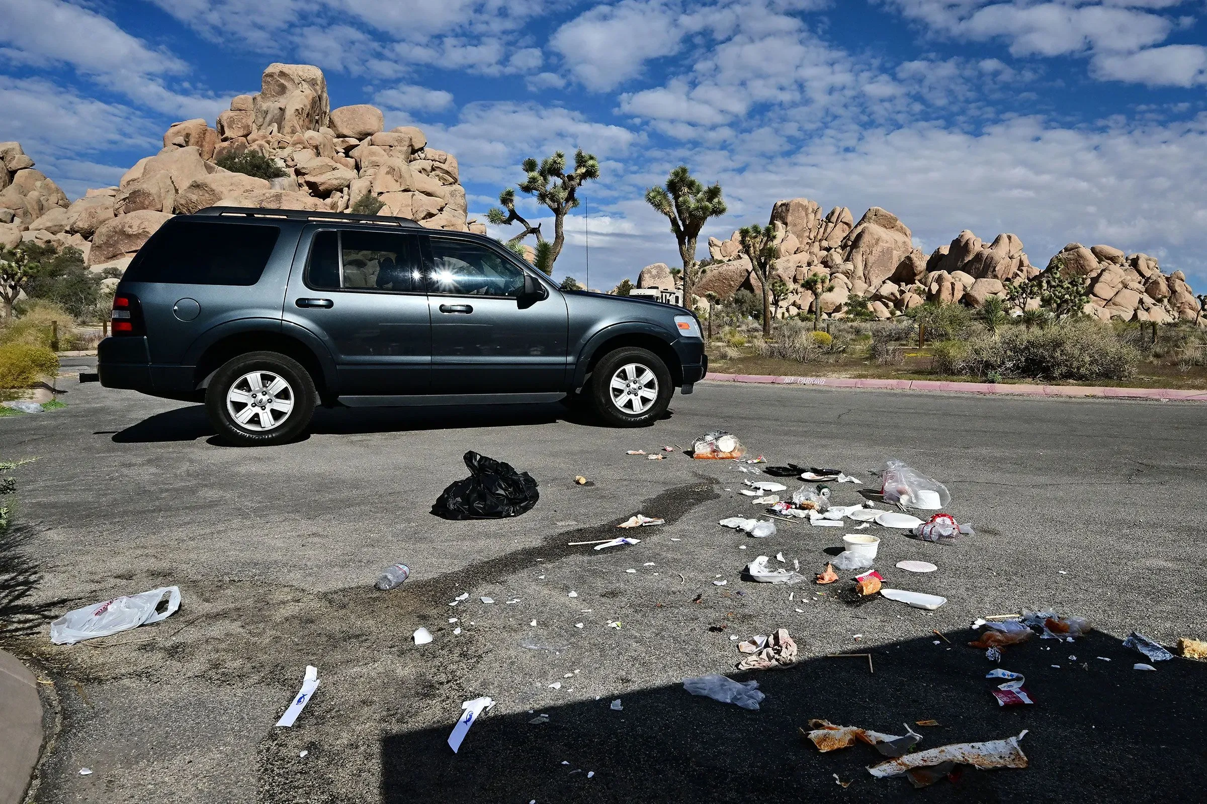 سيارة دفع رباعي متوقفة بجانب كومة من القمامة في منطقة طبيعية، مع صخور وجبال في الخلفية، تعكس آثار الإغلاق الحكومي على المتنزهات.