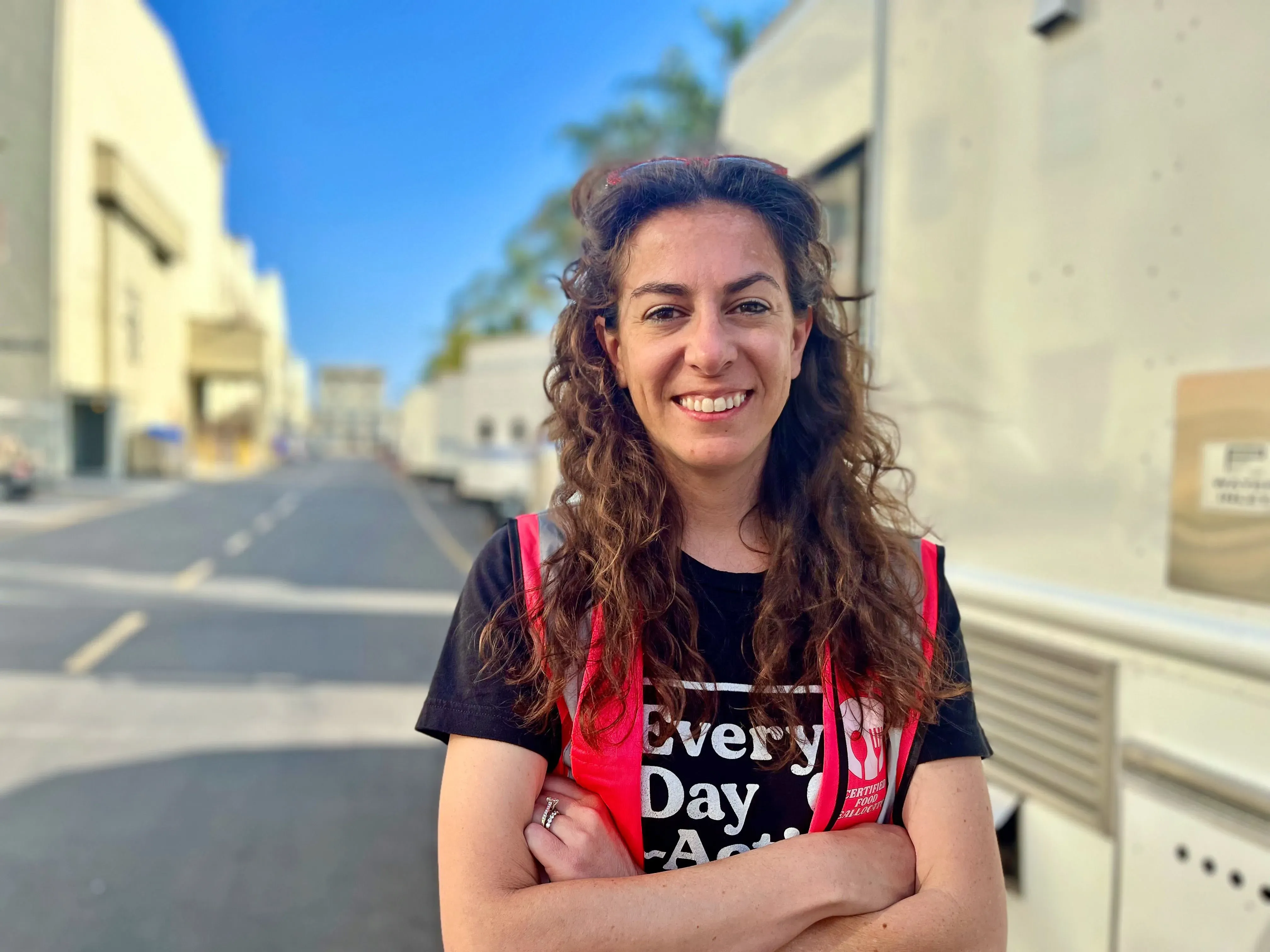 هيلاري كوهين، مؤسسة منظمة "كل يوم عمل"، تقف مبتسمة في موقع تصوير، مرتدية سترة حمراء، مع خلفية لمرافق الإنتاج.