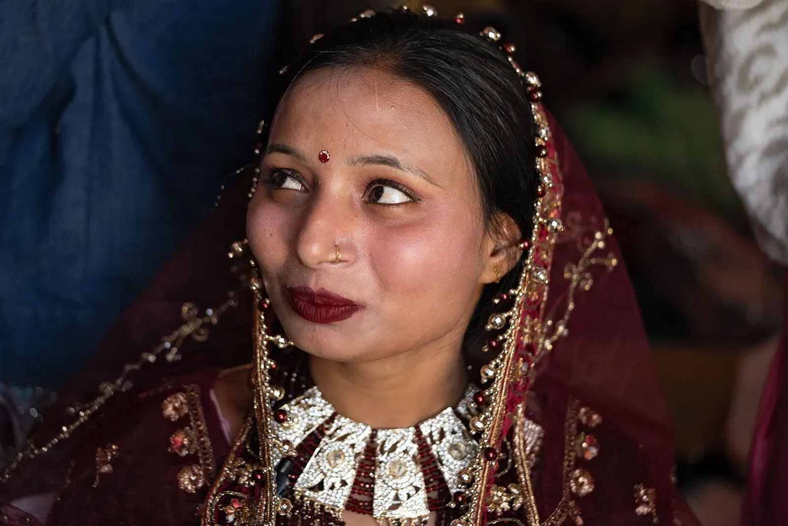 عروس ترتدي زياً تقليدياً مزيناً، وتظهر وهي تتلقى لمسات تجميلية قبل زفافها، مع تعبيرات مختلطة من السعادة والقلق.