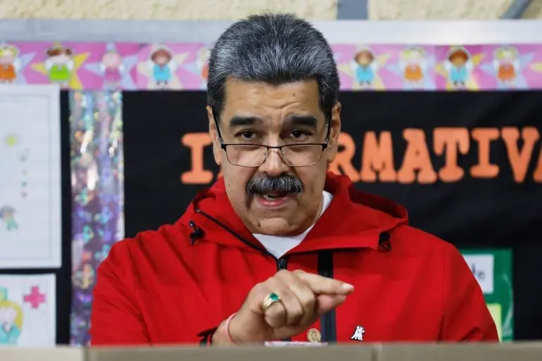 الرئيس الفنزويلي نيكولاس مادورو يتحدث في حدث عام، مرتديًا سترة حمراء، مع خلفية ملونة تعكس أجواء النشاط في البلاد.