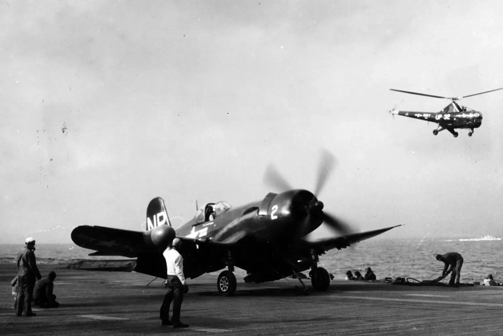 طائرة مقاتلة F4U Corsair أمريكية على متن حاملة طائرات خلال الحرب الكورية، مع هليكوبتر تحلق في الخلفية.