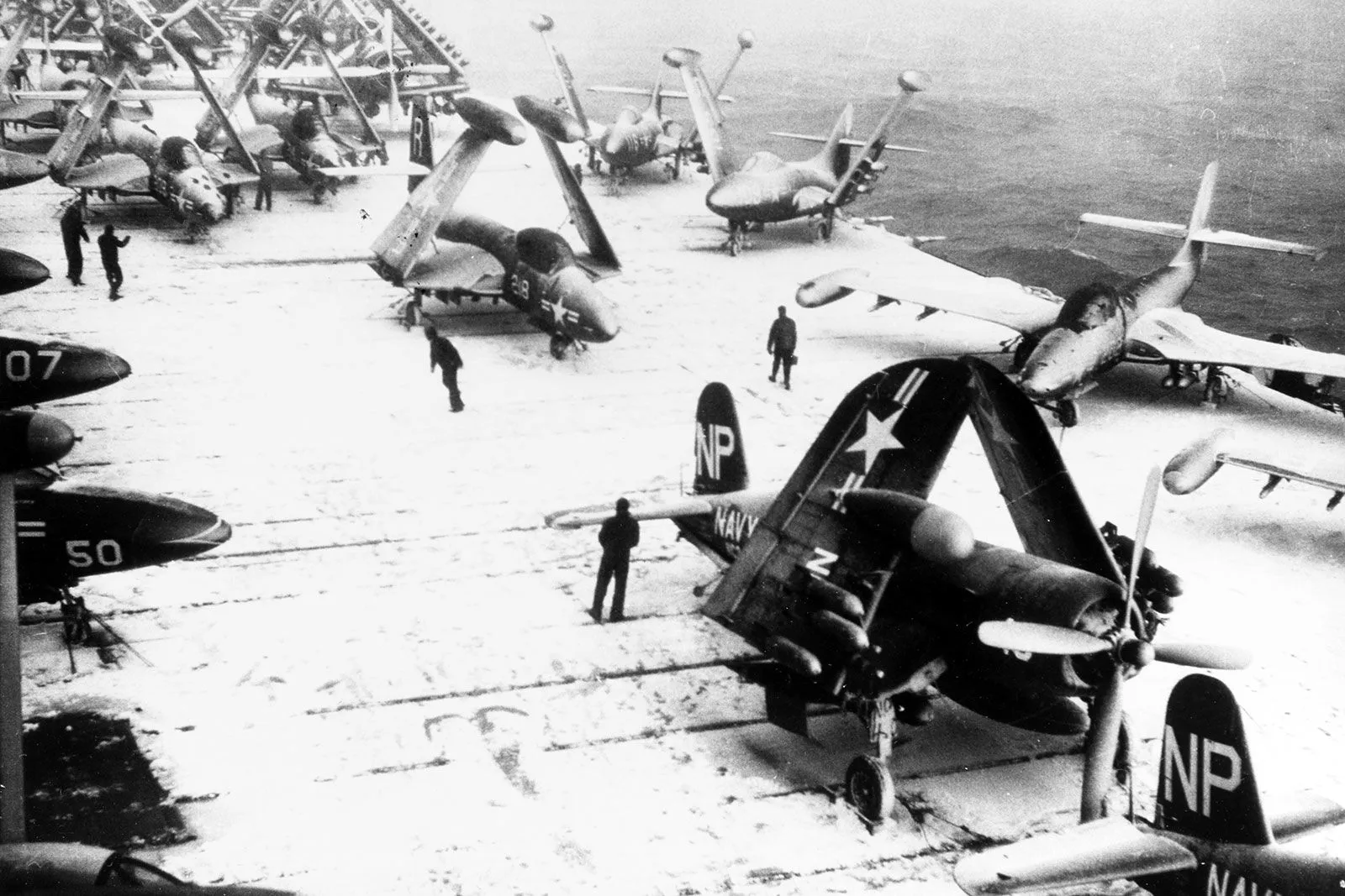 طائرات مقاتلة F4U Corsair مطوية الأجنحة على سطح حاملة طائرات أمريكية خلال الحرب الكورية، تظهر تفاصيل الطائرات وترتيبها استعداداً للطلعات الجوية.