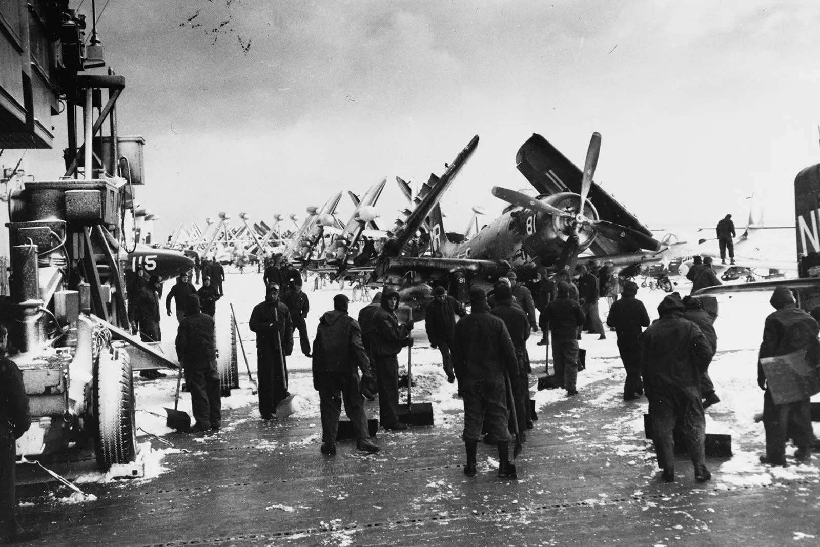 جنود على متن حاملة طائرات أمريكية في الشتاء أثناء الحرب الكورية، مع صف من طائرات F4U Corsair المميزة بأجنحتها المطوية.