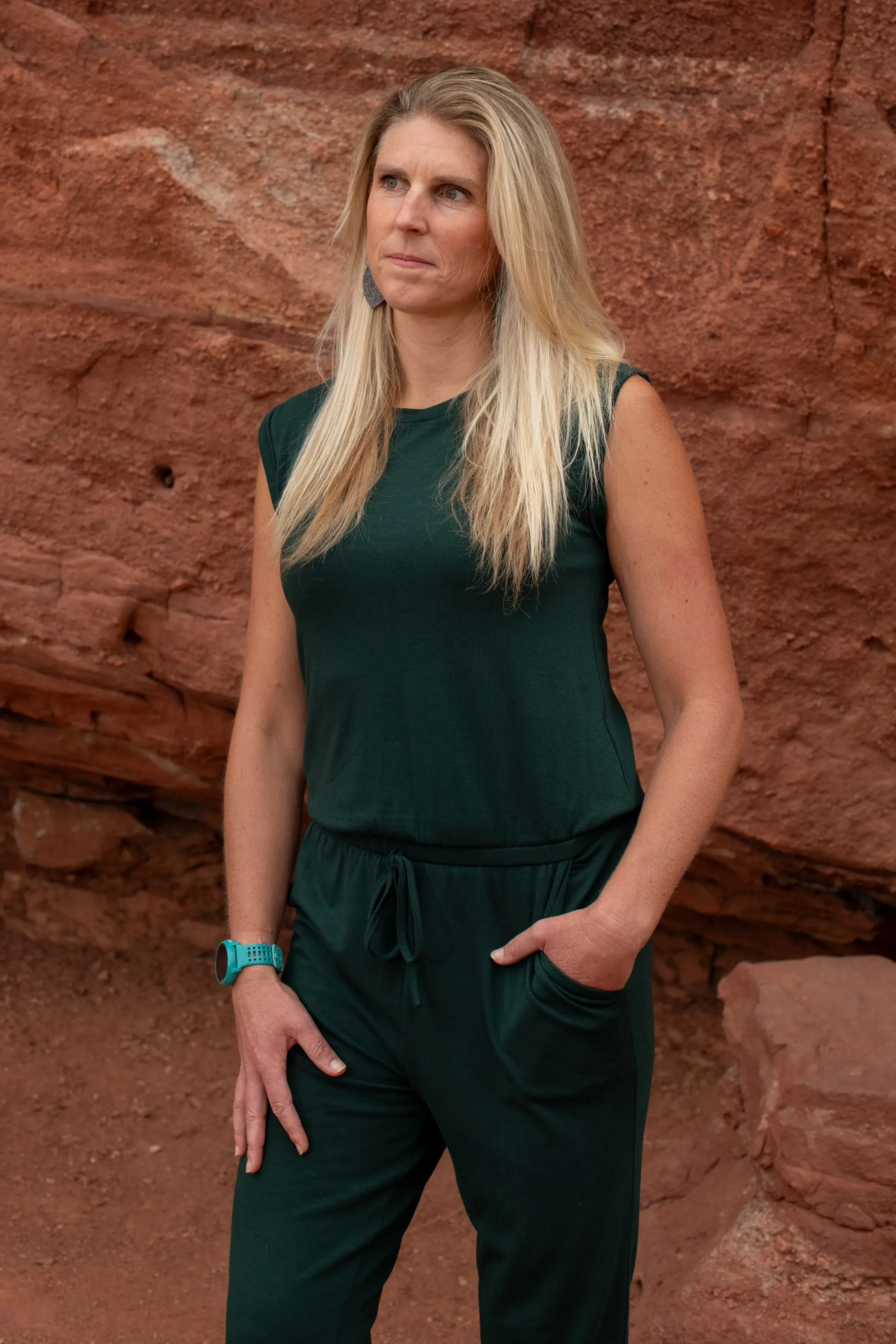 امرأة ترتدي زيًا رياضيًا باللون الأخضر تقف أمام صخور حمراء، تعكس القوة والصلابة في سياق قصة عائلية مأساوية.