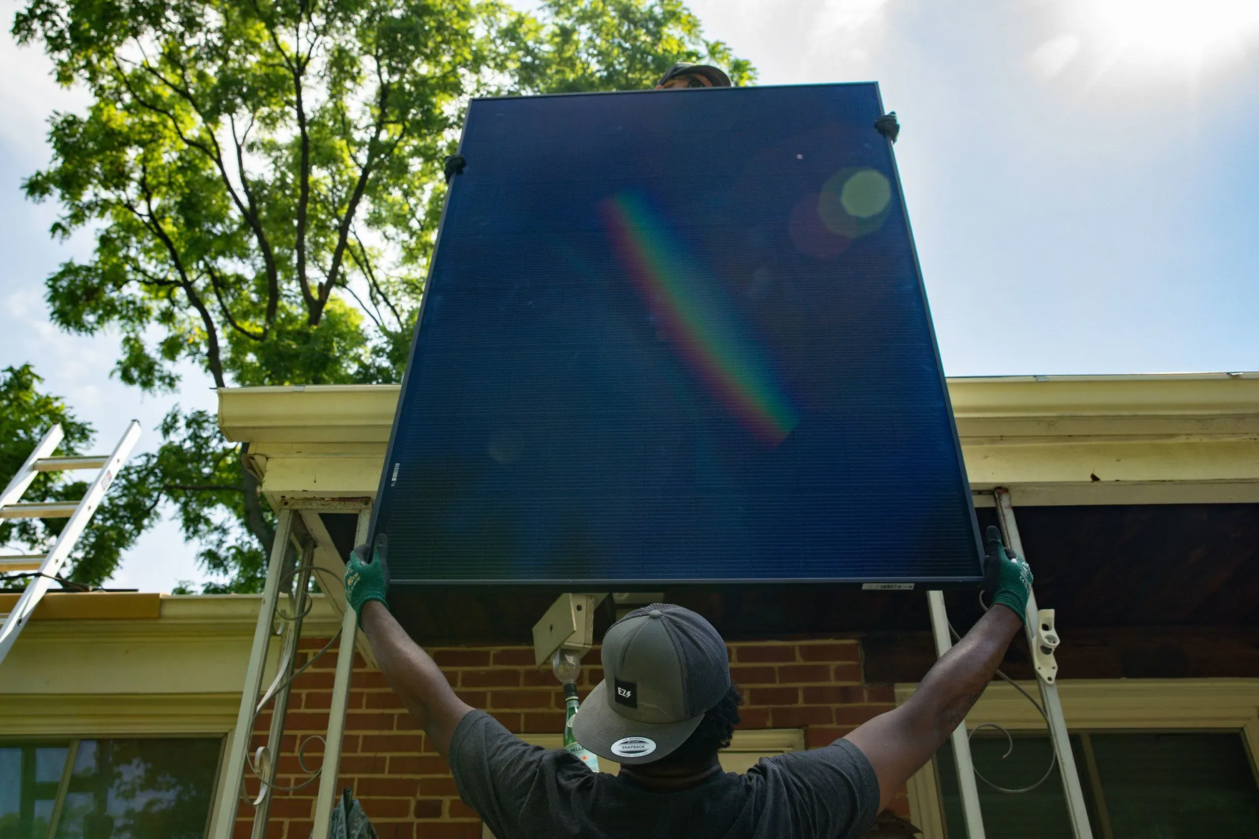 عامل يقوم بتركيب لوحة شمسية على سطح منزل، مما يعكس جهود تحسين كفاءة الطاقة في مواجهة ارتفاع تكاليف الكهرباء.