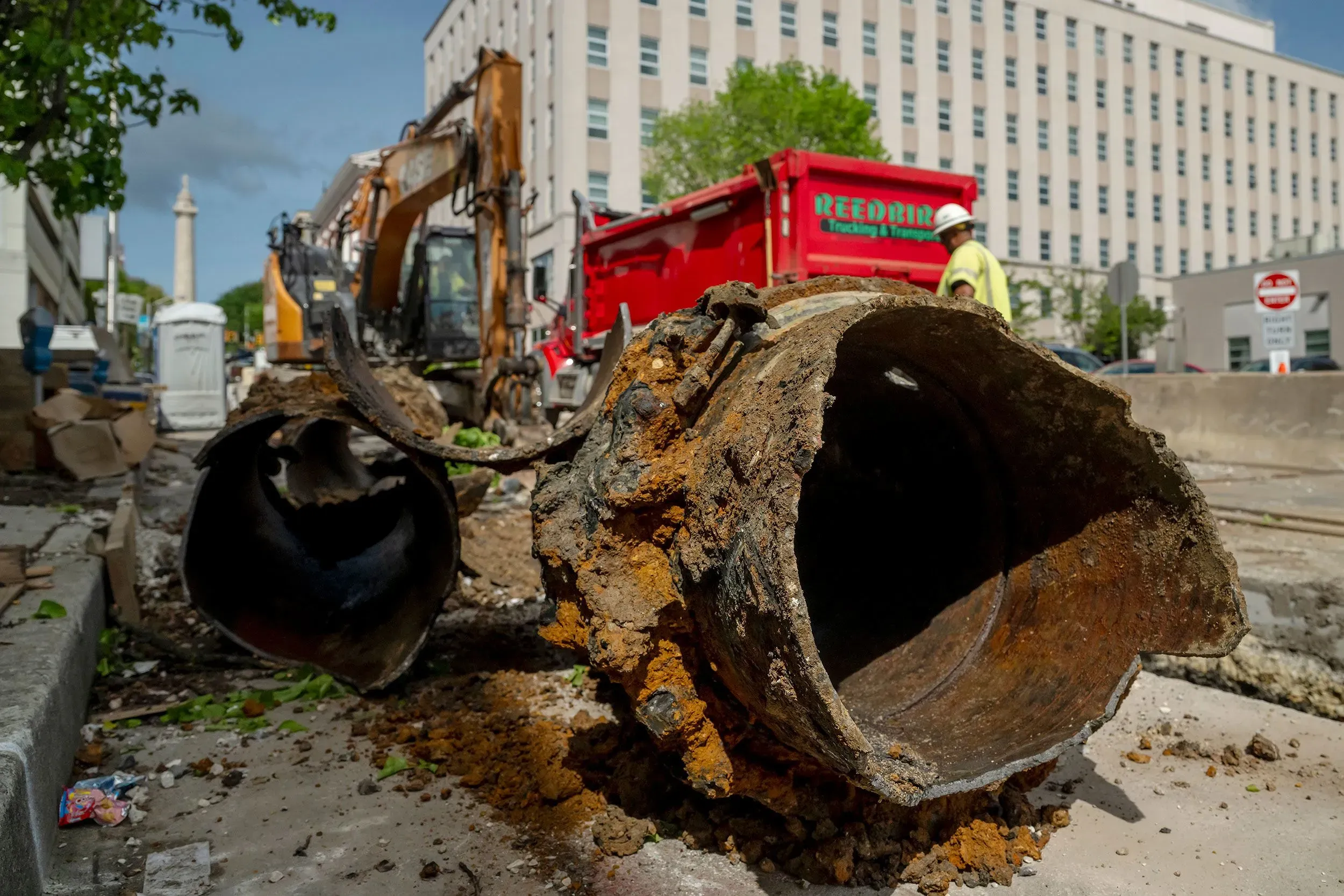 صورة تظهر أنابيب كهرباء قديمة ومتآكلة في موقع عمل، مع معدات بناء وخلفية حضرية، تعكس تحديات تحديث البنية التحتية الكهربائية.
