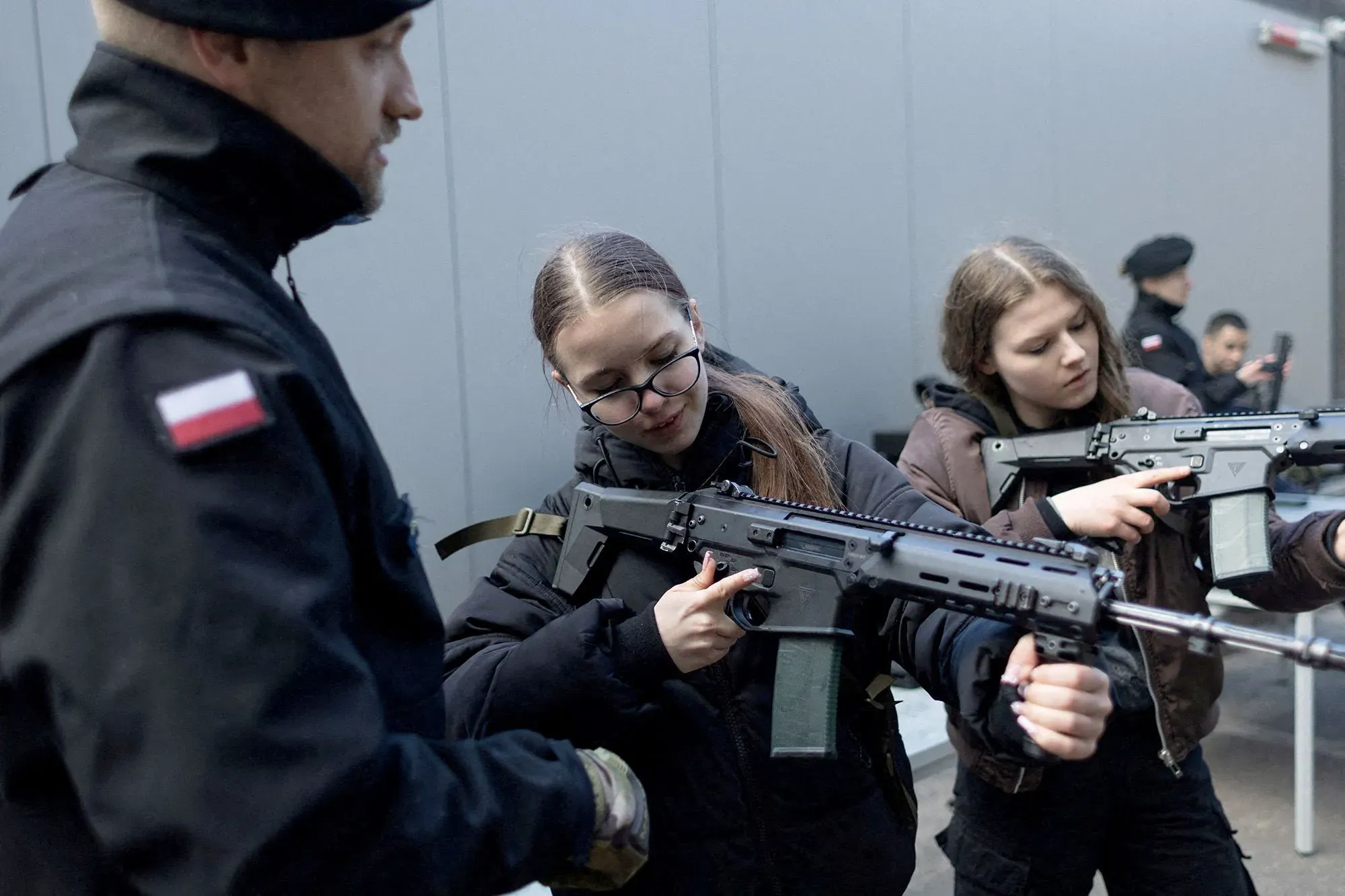 نساء يتدربن على استخدام أسلحة نارية في بيئة تعليمية، مع التركيز على أهمية الاستعداد للدفاع في سياق التوترات الجيوسياسية.