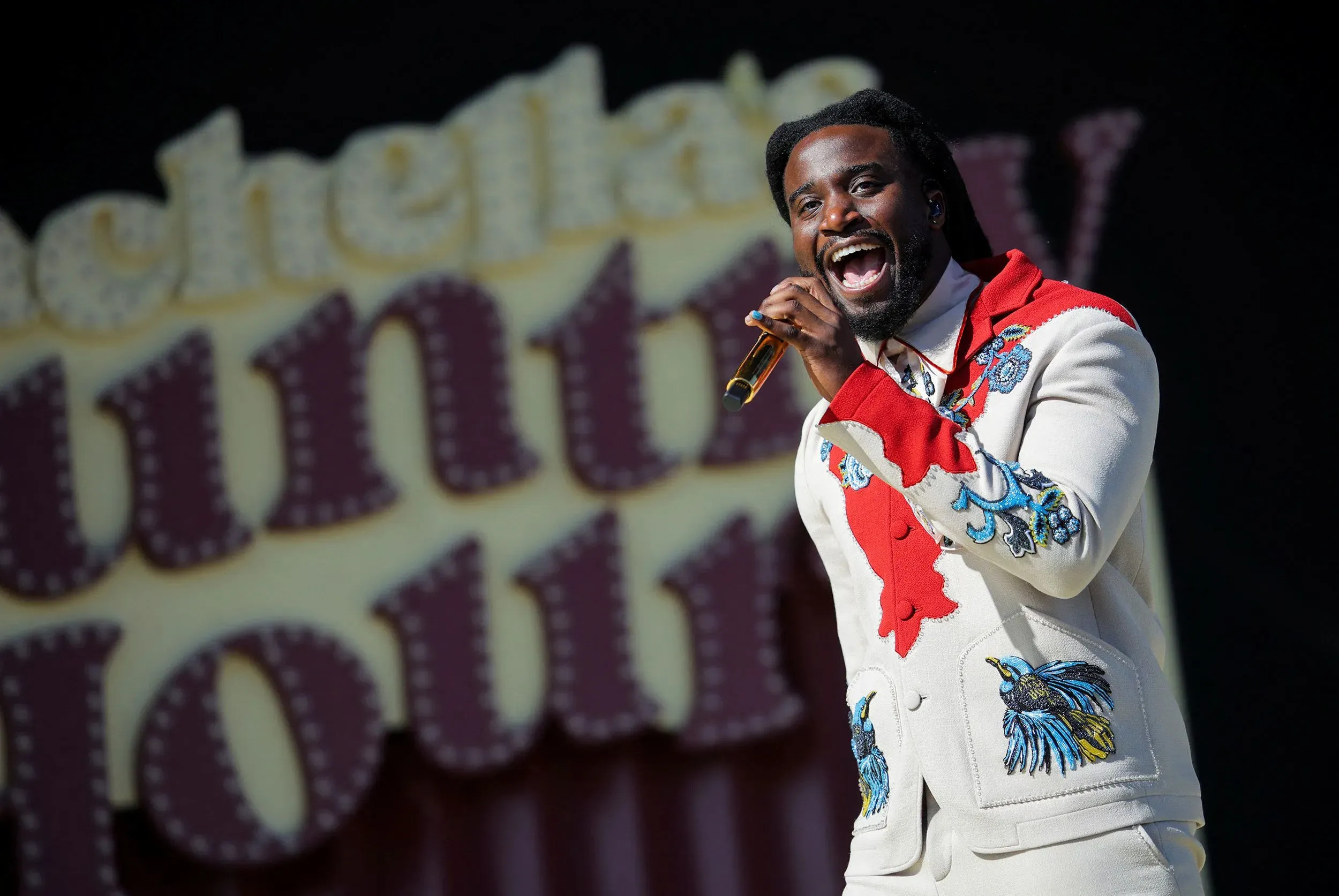 مغني يؤدي أغنية حماسية على المسرح خلال مهرجان، مع خلفية ملونة تحمل اسم المهرجان، تعكس أجواء الصيف والموسيقى.