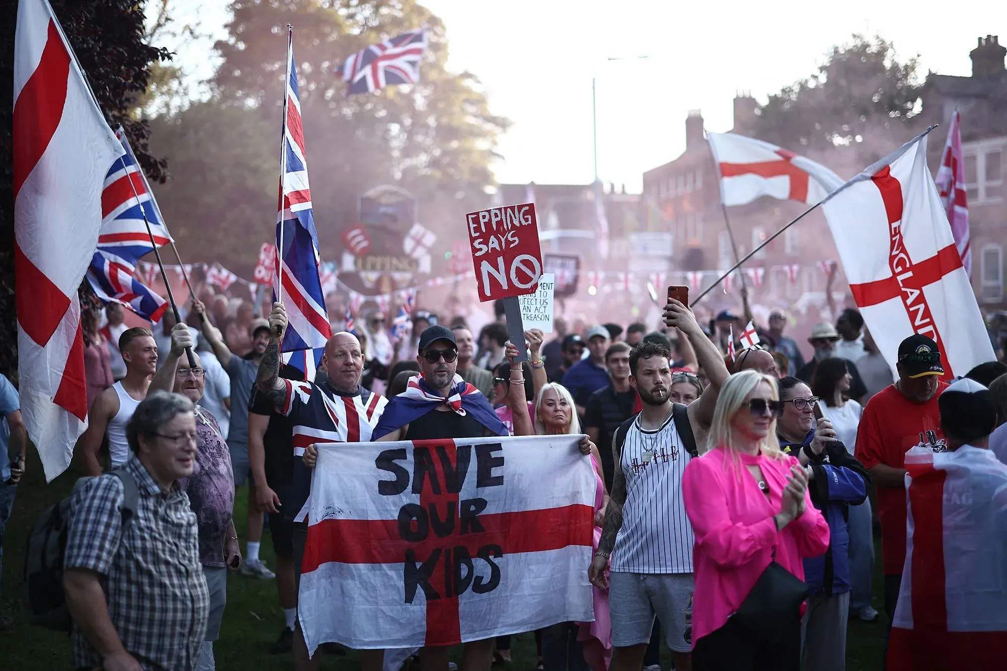 تجمع حشود من المتظاهرين في إيبينغ، يحملون أعلام المملكة المتحدة وعلم إنجلترا، مع لافتات تعبر عن مشاعر وطنية متباينة.