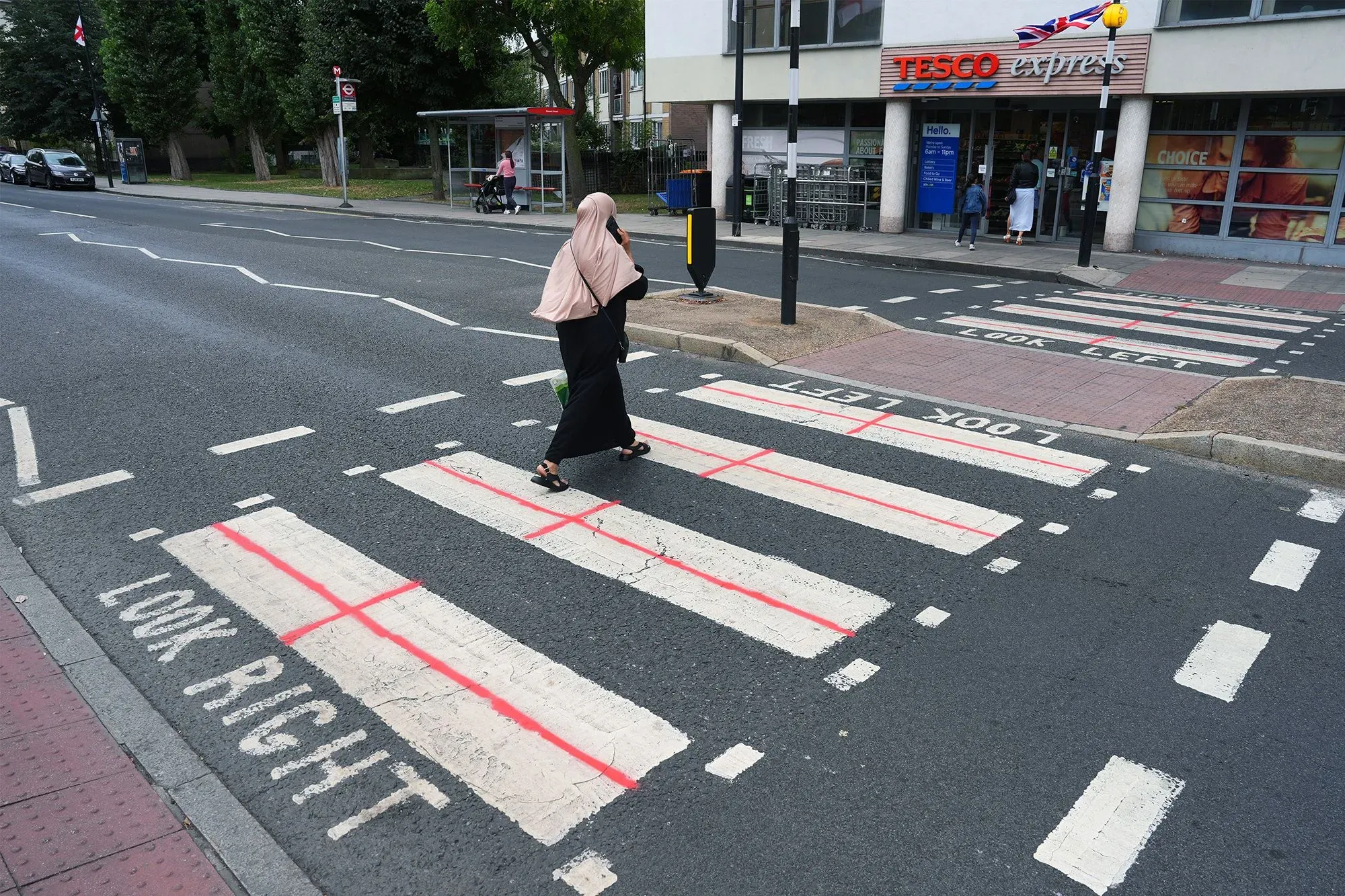 امرأة ترتدي الحجاب تعبر ممر المشاة في مدينة إنجليزية، حيث تظهر علامات "انظر يمينًا" و"انظر يسارًا" مرسومة باللون الأحمر.