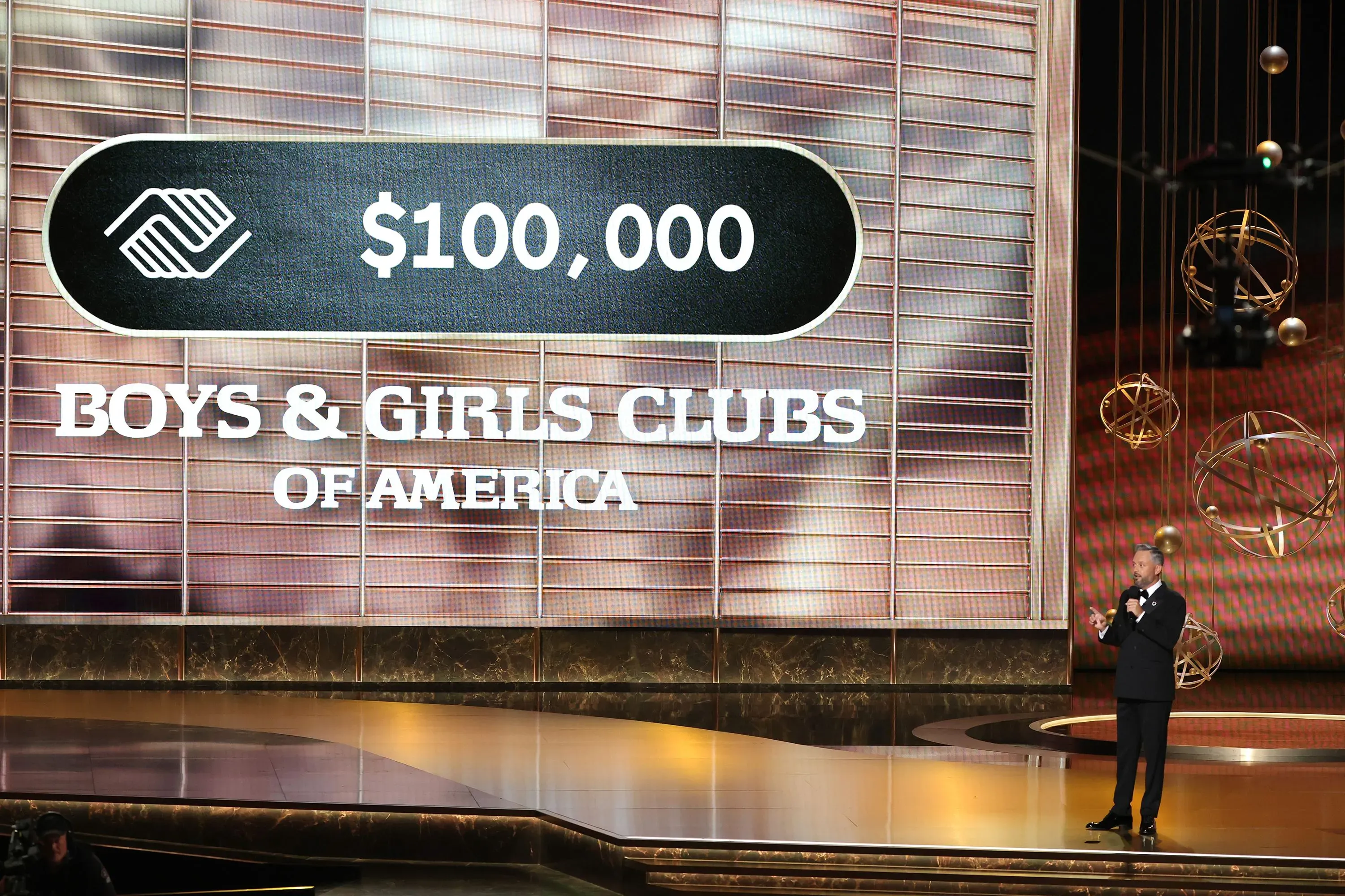 تبرع بقيمة 100,000 دولار لنادي الأولاد والبنات في أمريكا، مع تقديم أحد المتحدثين على المسرح خلال حفل توزيع جوائز إيمي 2025.