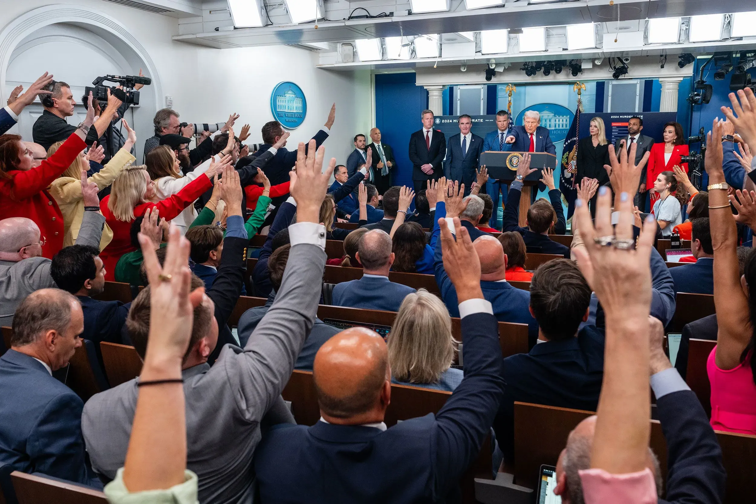 مؤتمر صحفي في البيت الأبيض حيث يرفع الصحفيون أيديهم لطرح الأسئلة، مع وجود الرئيس دونالد ترامب يتحدث في المقدمة.