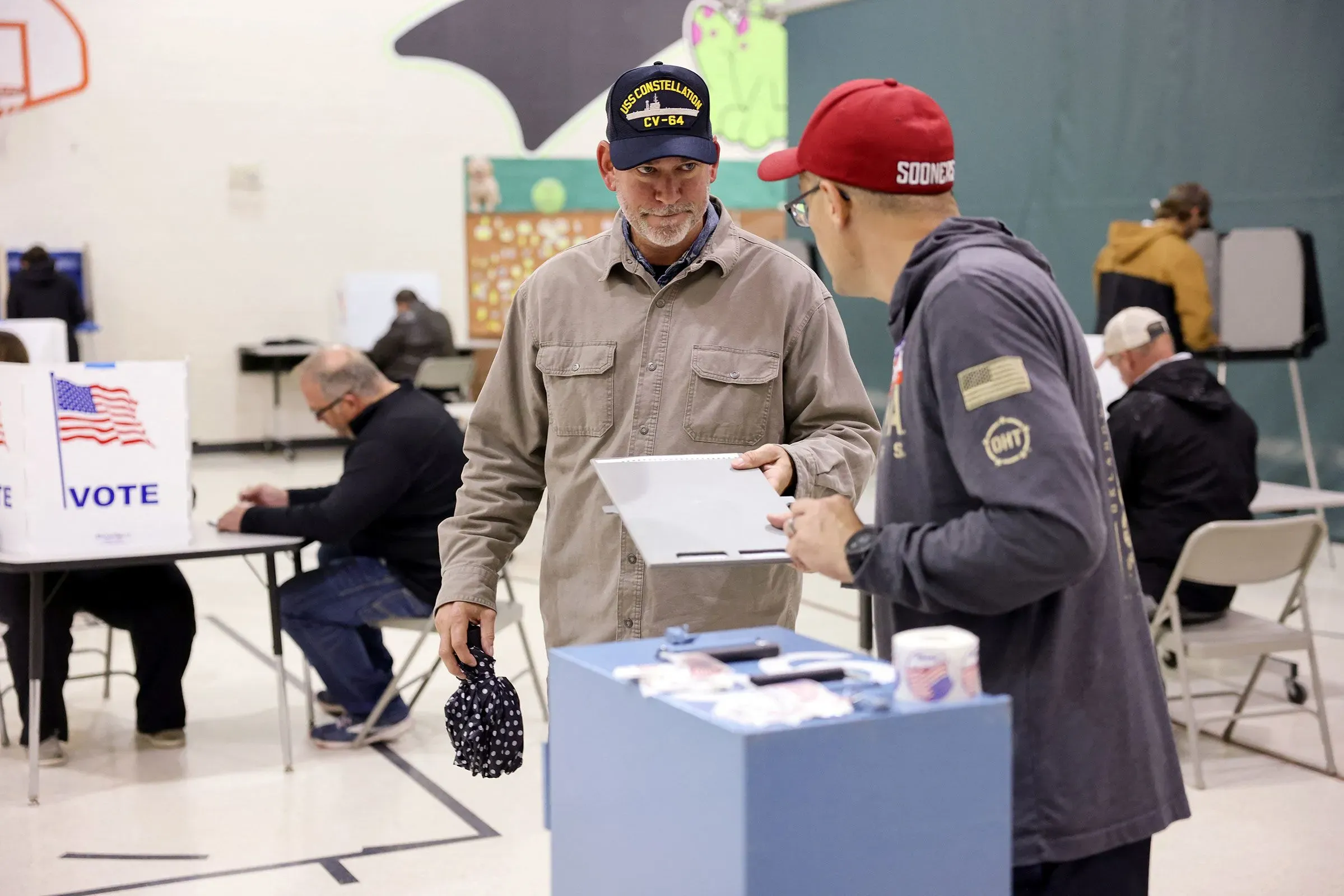 ناخبون يتبادلون الحديث داخل مركز اقتراع في نبراسكا، مع وجود صناديق اقتراع خلفهم، مما يعكس أجواء الانتخابات التمهيدية.