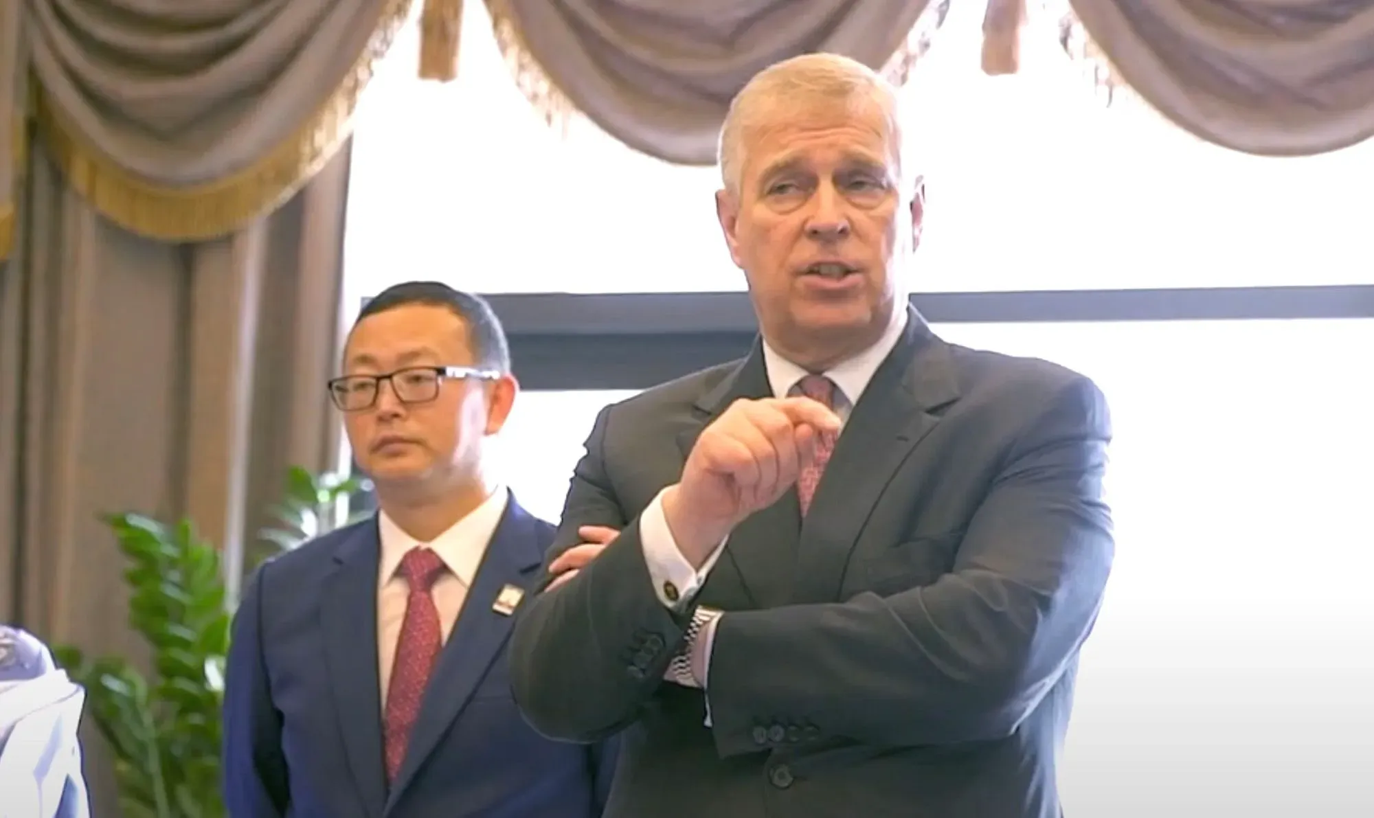 الأمير أندرو يتحدث خلال حدث رسمي، بينما يقف رجل آخر يرتدي نظارات خلفه، في سياق الفضيحة المتعلقة بجيفري إبشتاين.