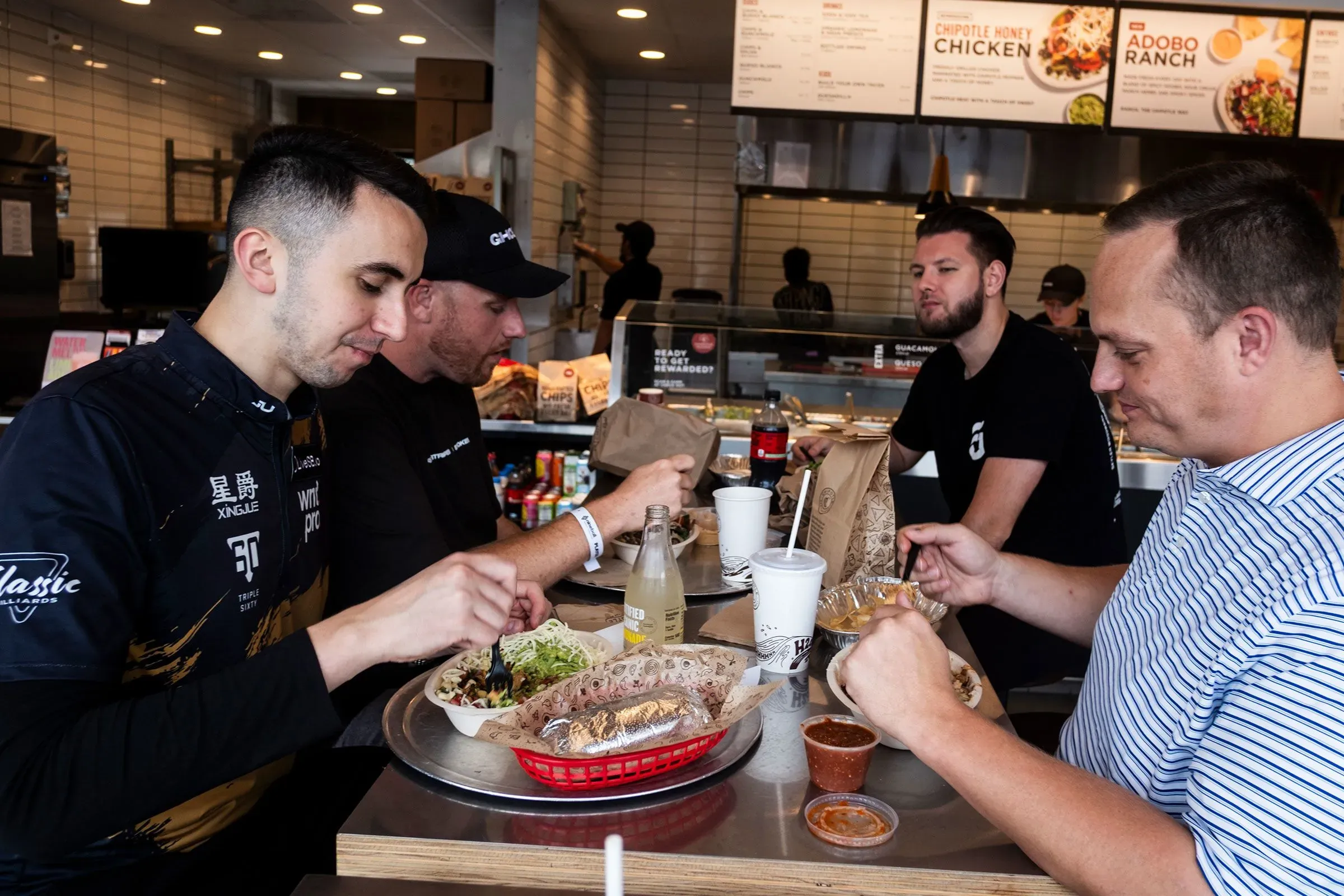 غورست وأصدقاؤه يتناولون الطعام في مطعم، مع أطباق مليئة بالخضروات واللحوم، بينما يتمتعون بأجواء غير رسمية بعد المنافسة.