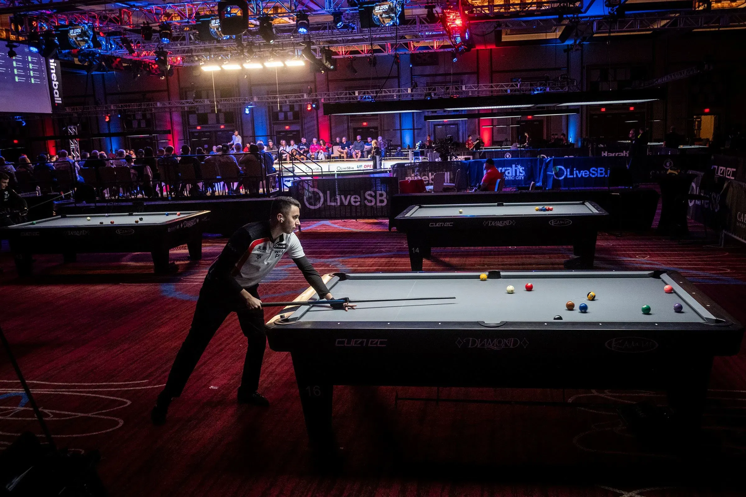 لاعب بلياردو يتنافس في بطولة الولايات المتحدة المفتوحة، مع كرات بلياردو على الطاولة وجمهور في الخلفية.