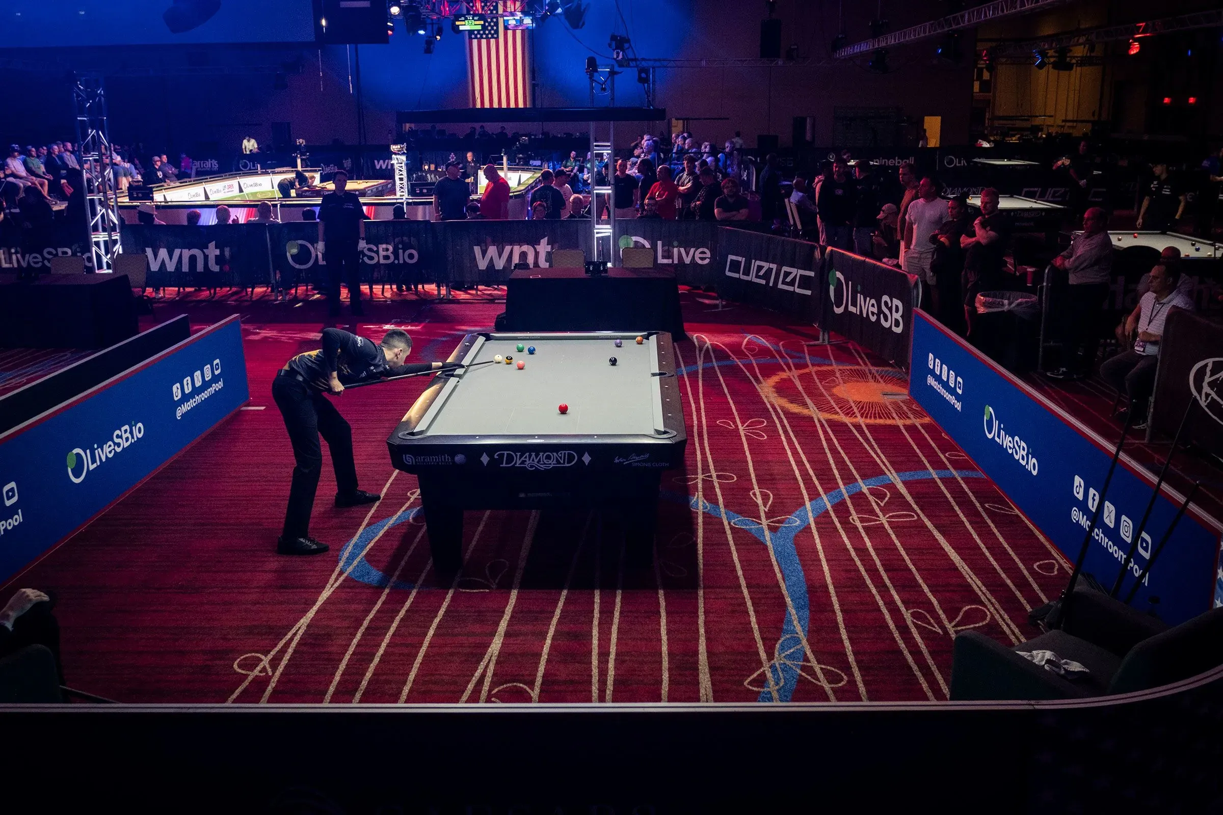 لاعب بلياردو يتنافس في بطولة الولايات المتحدة المفتوحة، مع جمهور كبير في الخلفية وأعلام أمريكية تزين المكان.