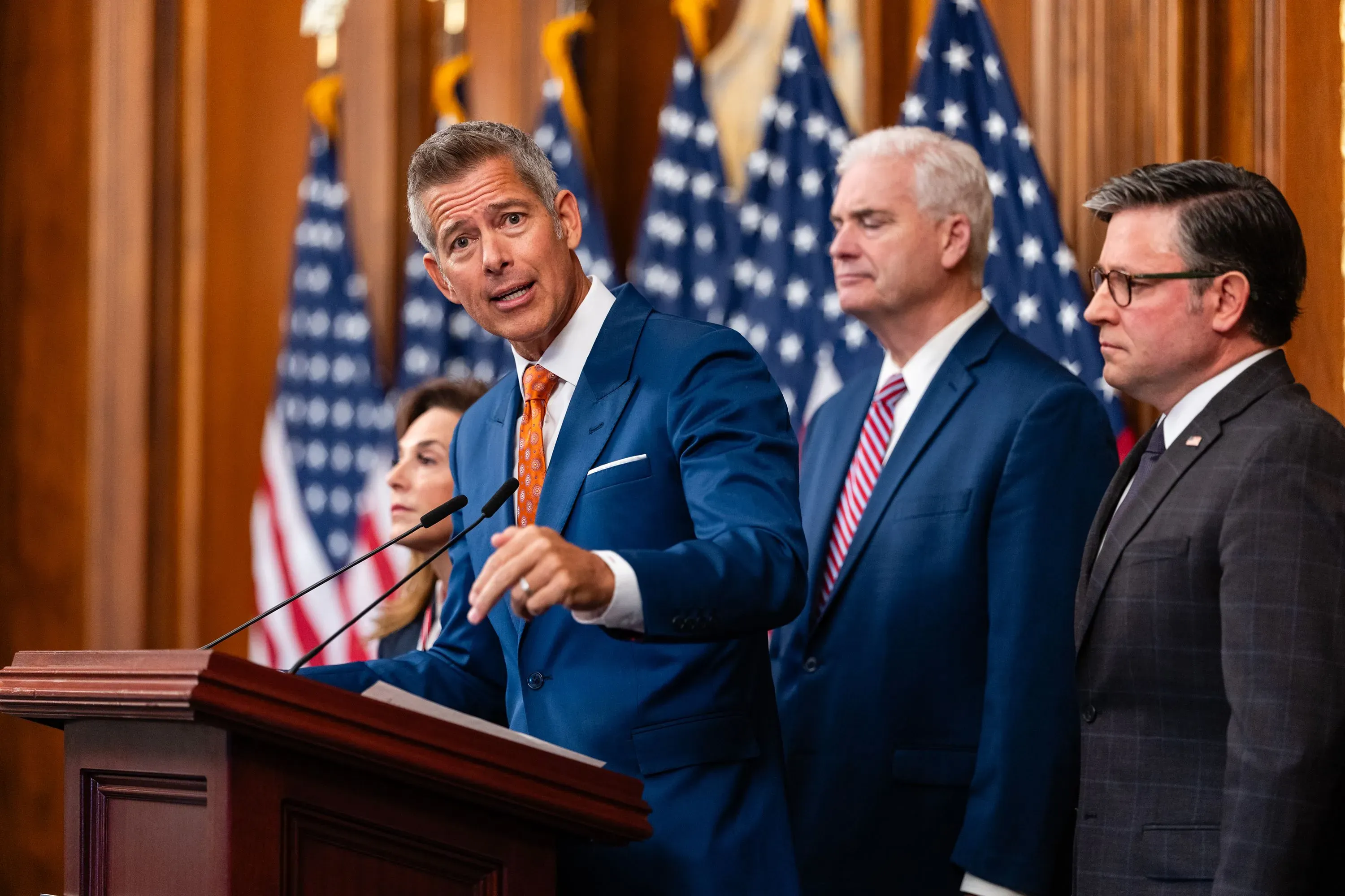 مشرعون يتحدثون خلال مؤتمر صحفي حول أزمة مراقبة الحركة الجوية في الولايات المتحدة، مع وجود أعلام خلفهم.