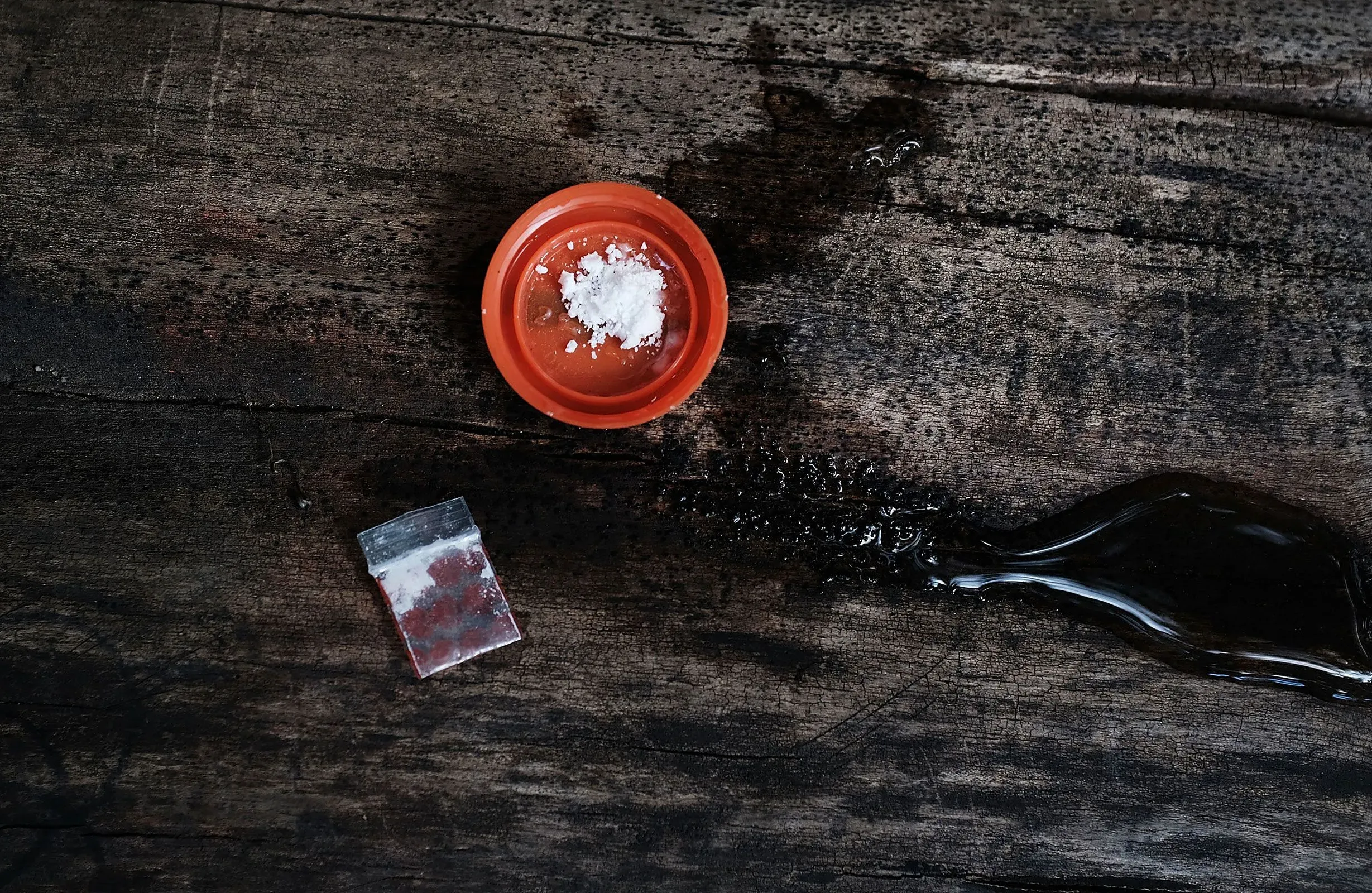 صحن صغير يحتوي على مسحوق أبيض بجانب كيس بلاستيكي فارغ، موضوعة على سطح خشبي، تعكس موضوع الحرب على المخدرات وتأثيرها.