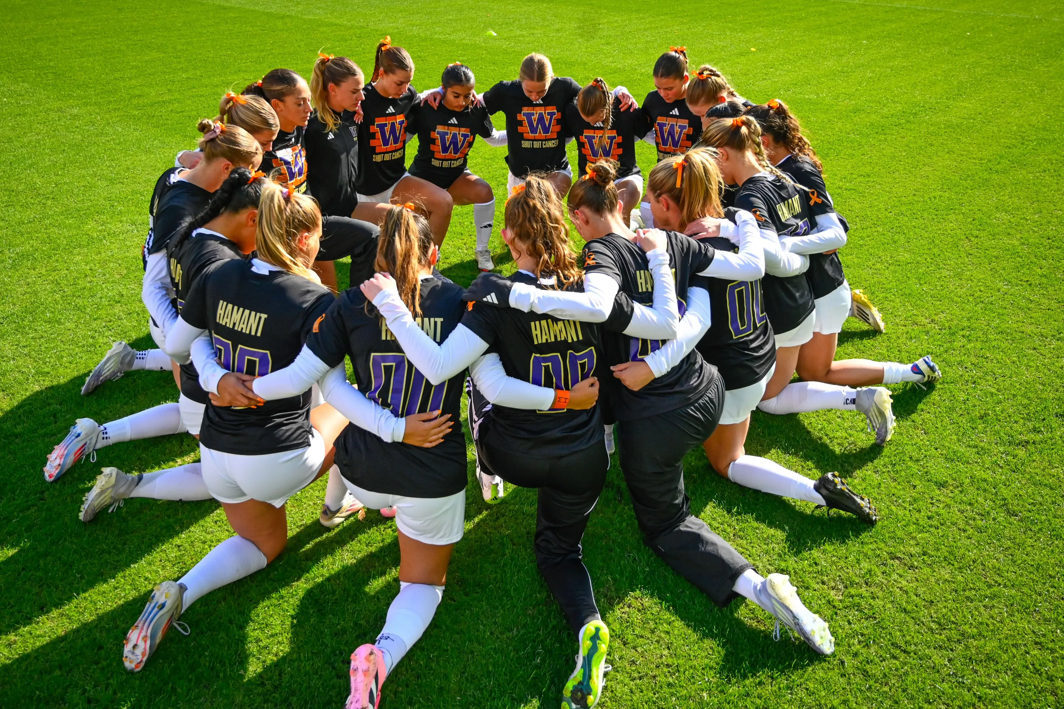 فريق كرة القدم النسائي في جامعة واشنطن يجتمع في حلقة، مع التركيز على القمصان التي تحمل اسم "هامانت"، في لحظة تأمل بعد خسارة مؤلمة.