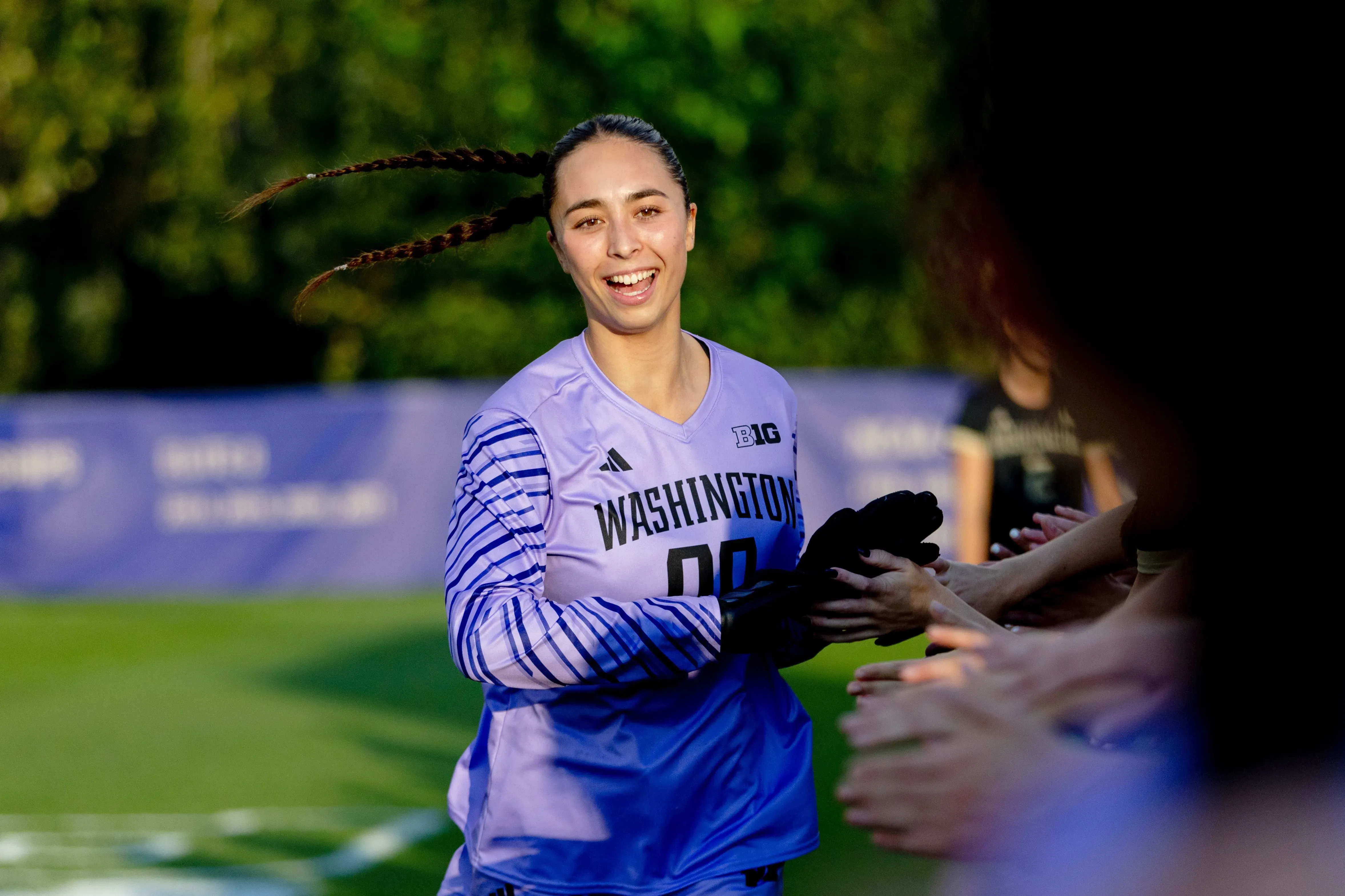 لاعبة كرة القدم ميا هامانت تبتسم أثناء تلقي التحية من الجماهير، مرتدية زي فريق جامعة واشنطن، تعكس روح الفريق والتفاؤل.