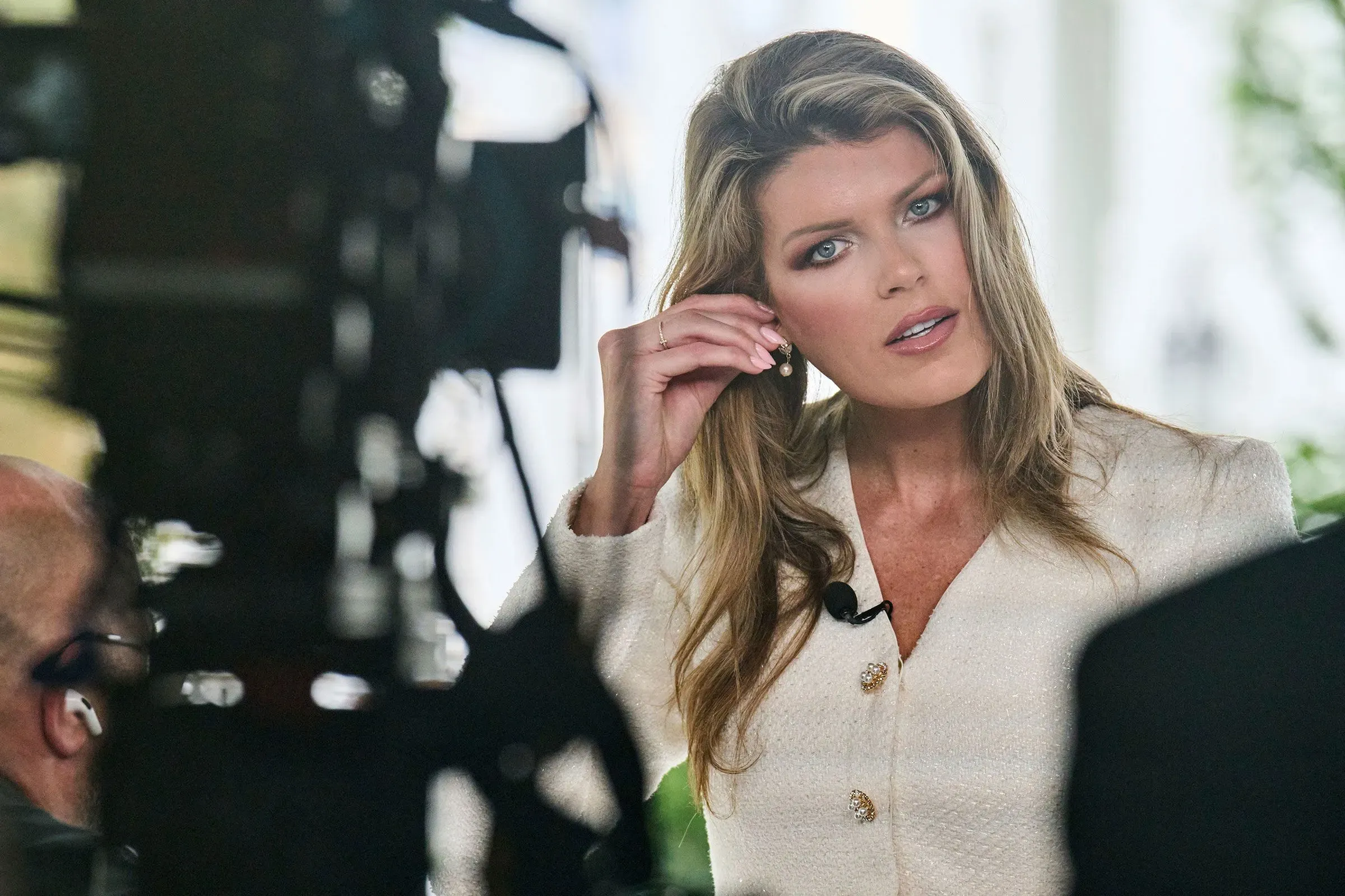 امرأة ترتدي سترة بيضاء، تتحدث بحماس أمام الكاميرا في بيئة إعلامية، تعكس تأثير إد مارتن في وزارة العدل.